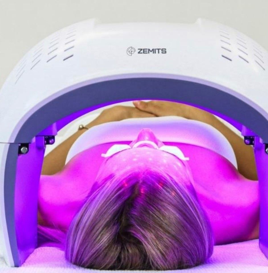 A woman is laying under a blue led light device.