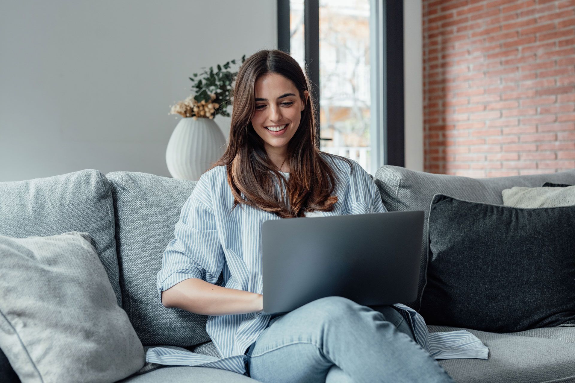 A woman is sitting on a couch using a laptop computer.