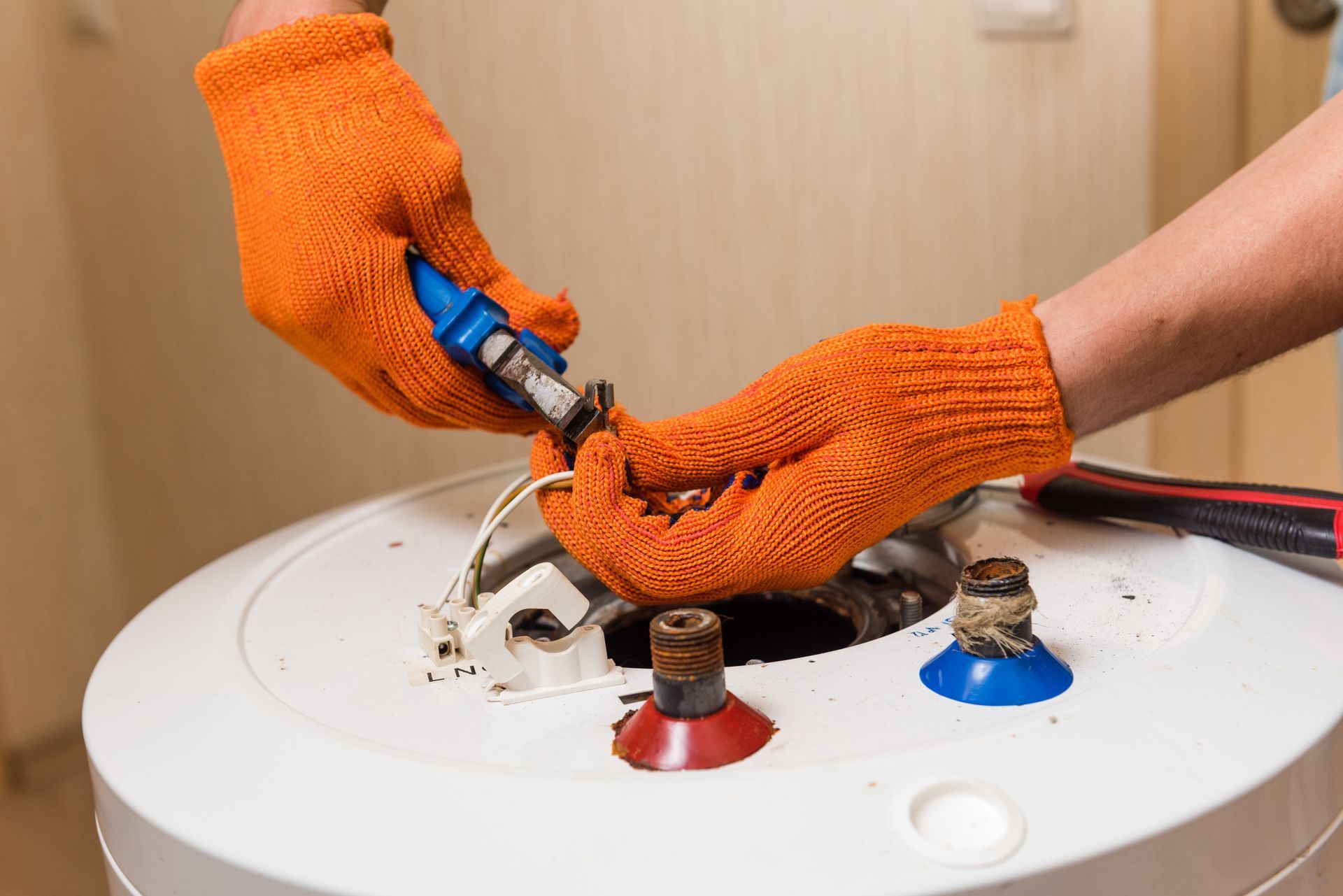 Gloved hands using a wrench to connect hoses on top of a white water heater tank
