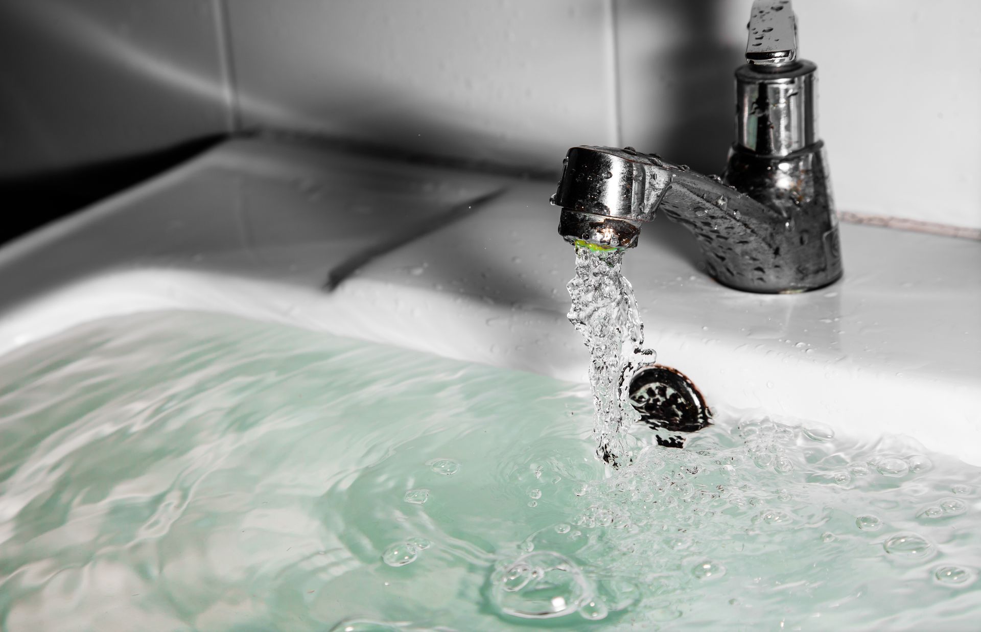 Water running from a faucet into a sink, filling with pale green-tinted water.