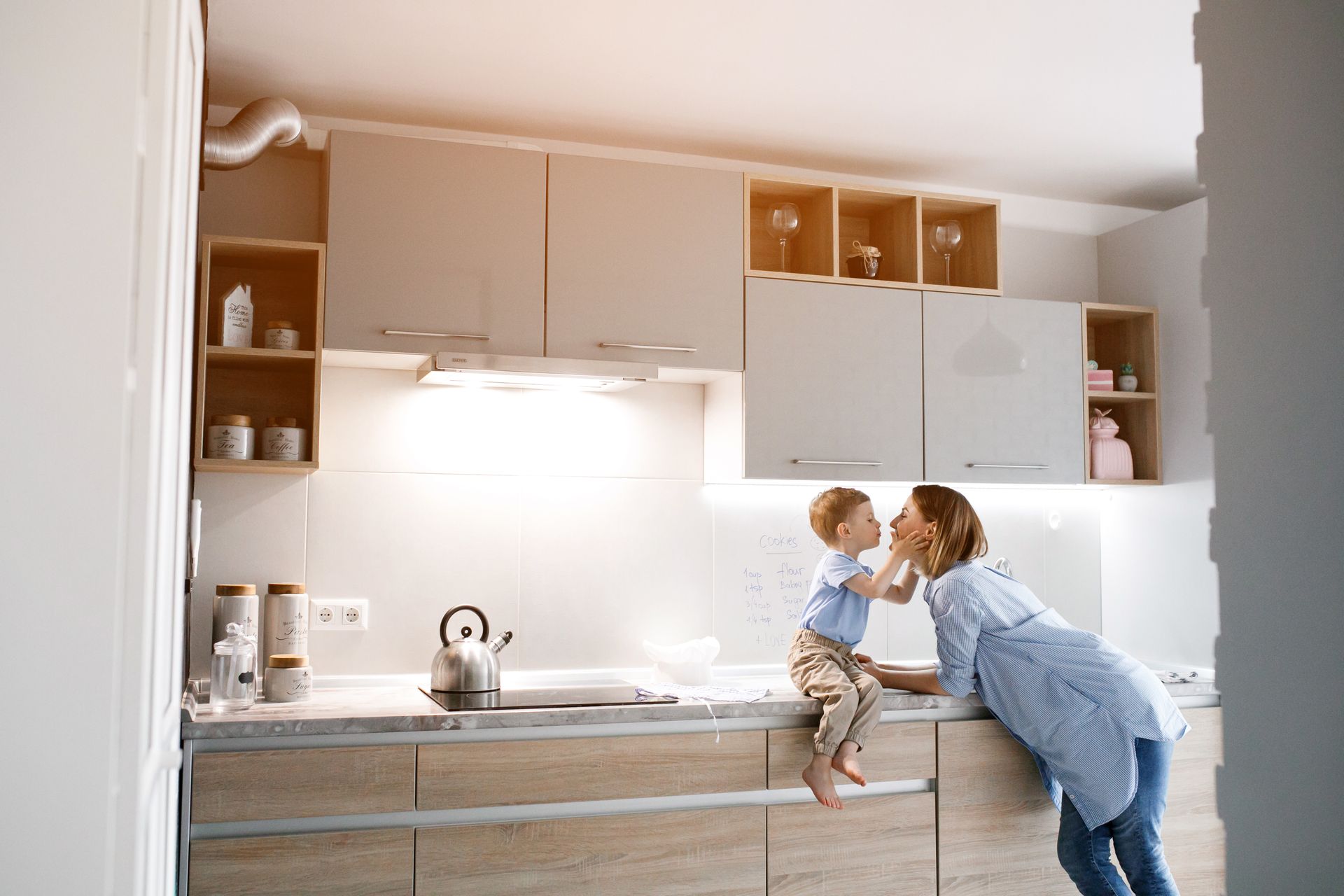 Adult helping a child in a bright modern kitchen, reaching up near the counter.