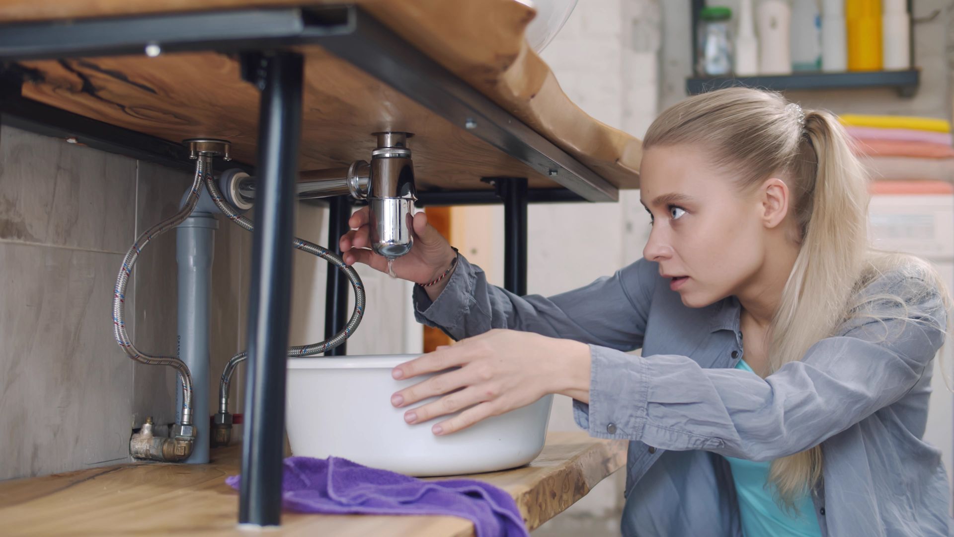Woman installing a kitchen filter under a sink, holding a wrench and adjusting plumbing pipes.