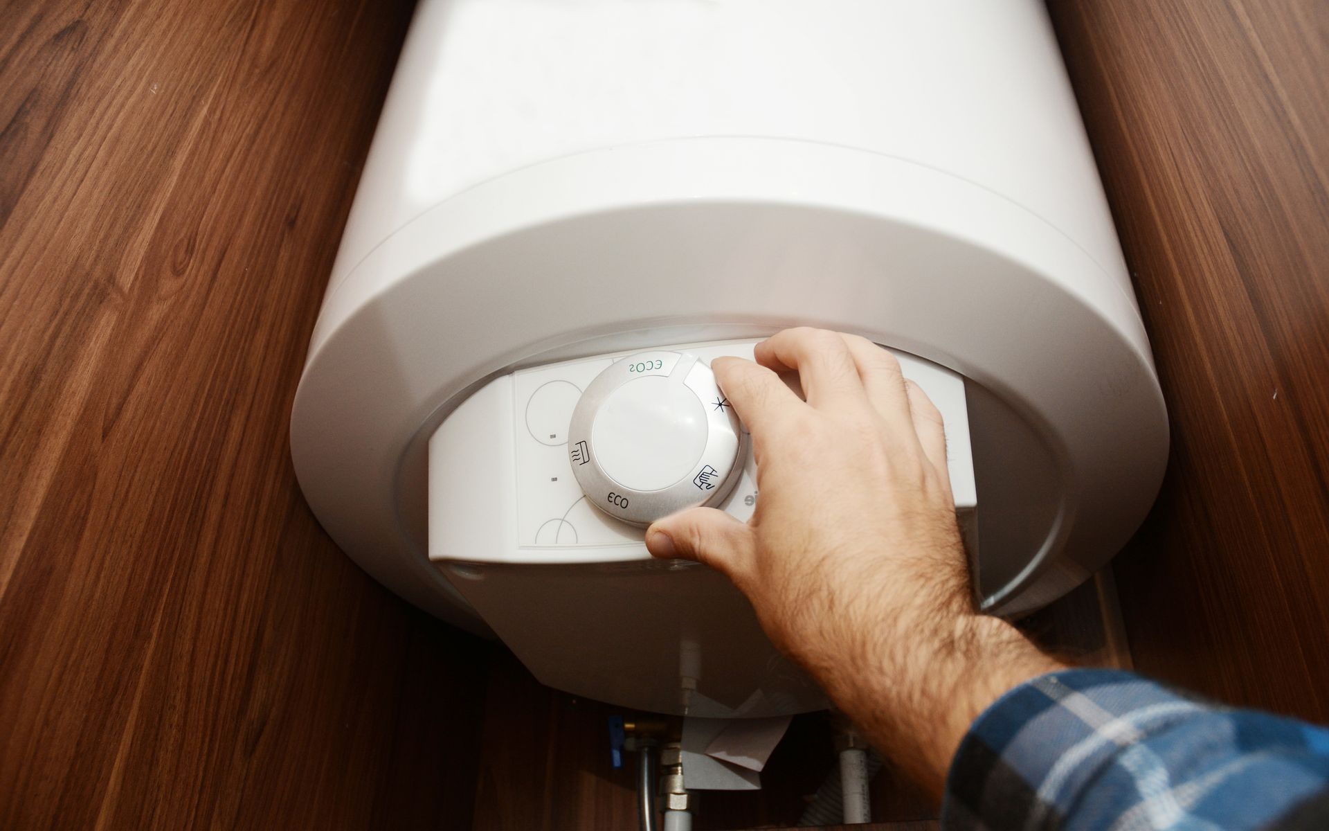 Hand turning the temperature dial on a white wall heater mounted above a wooden floor