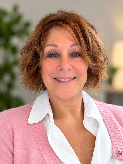Smiling person in a pink cardigan and white blouse against a softly blurred indoor background