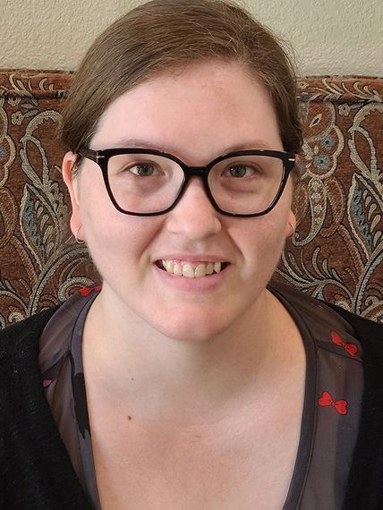 Person with glasses smiling in front of a patterned couch.