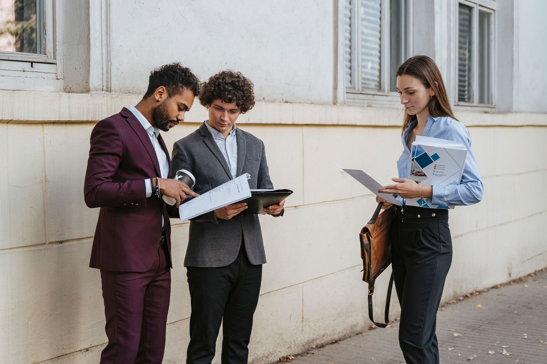 Three people standing outside a building, reviewing papers and a tablet.