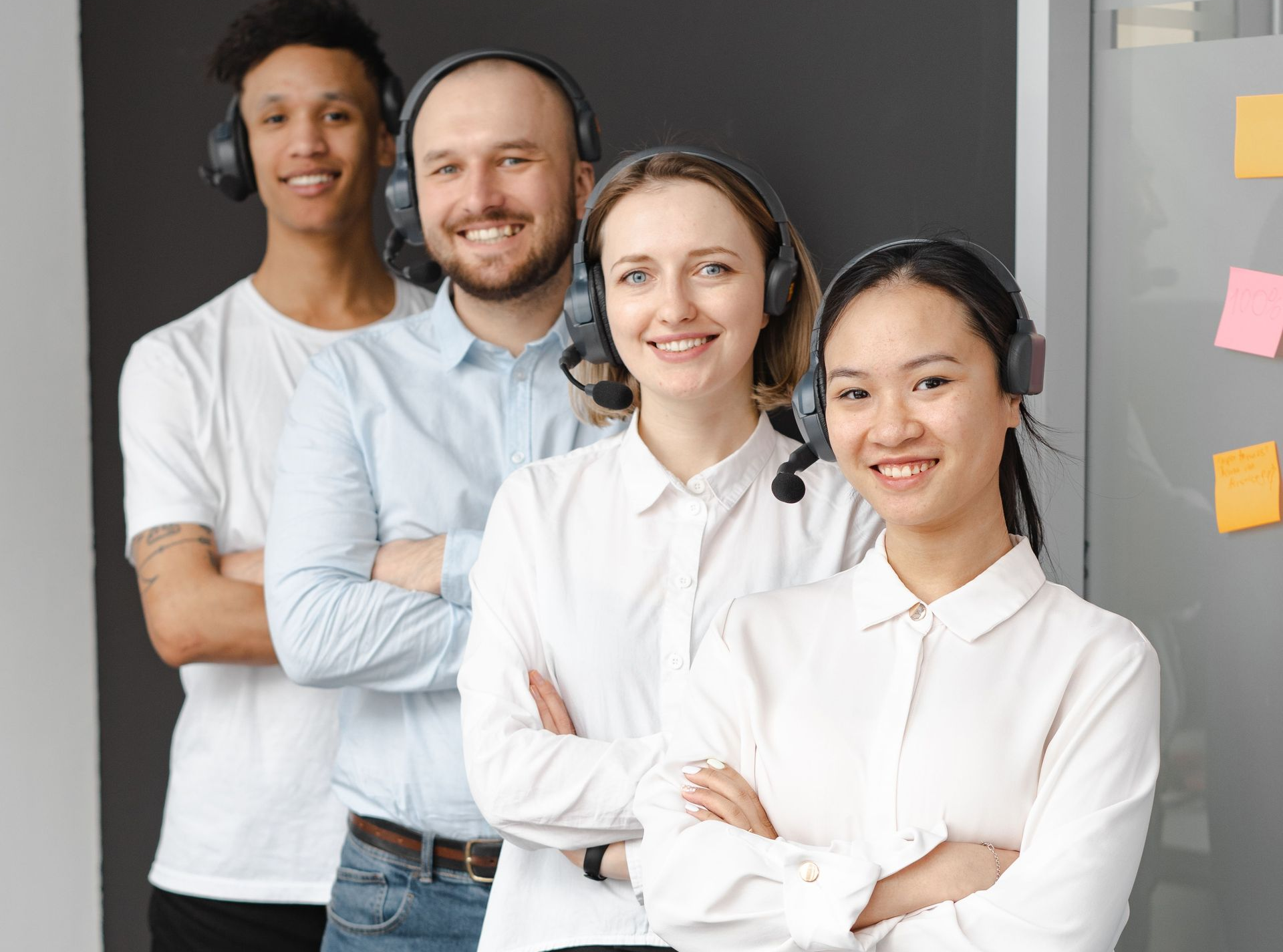 Four smiling office workers in headsets standing together in a modern office