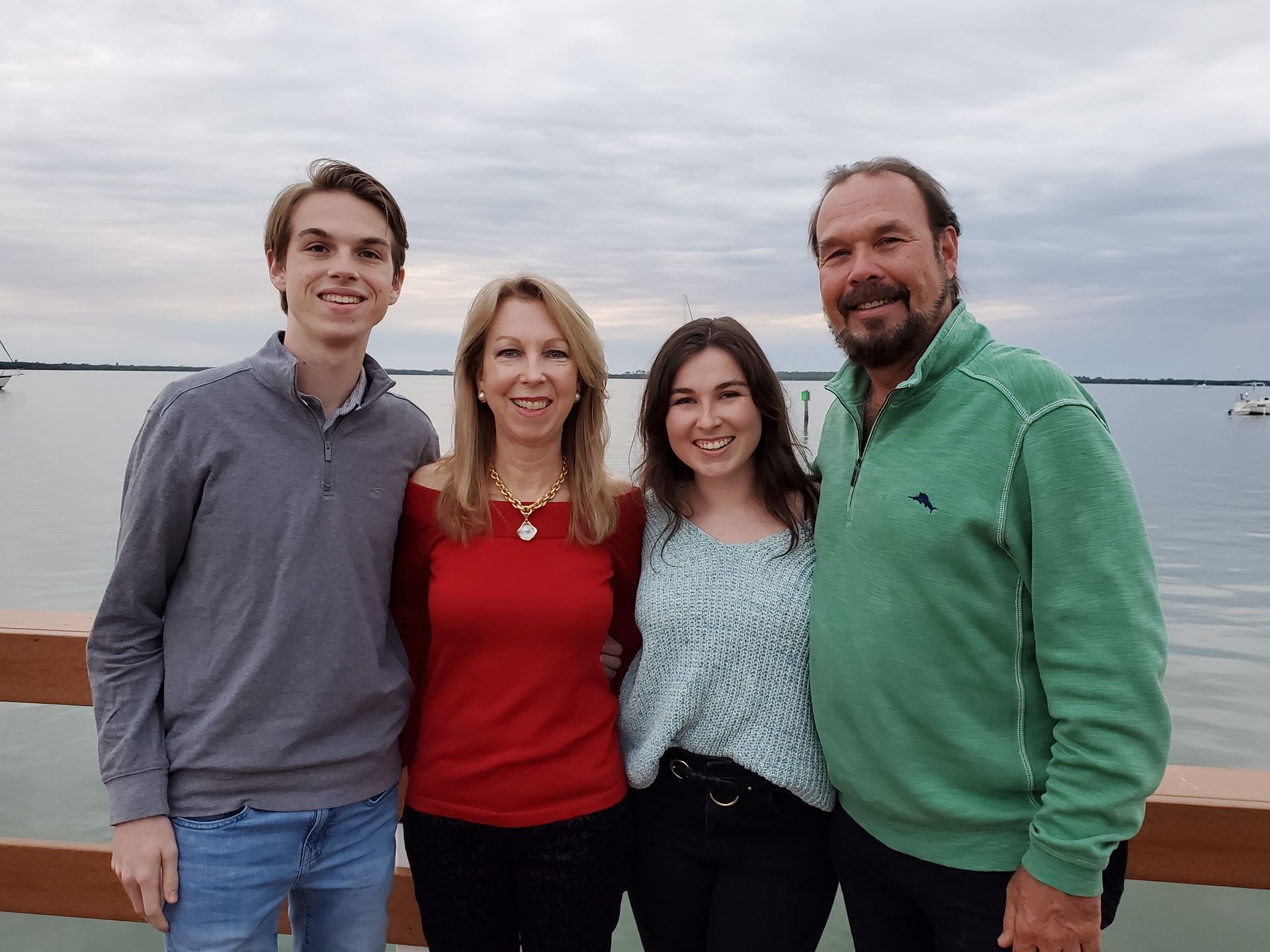 Four people standing close together outdoors by the water, smiling at the camera.
