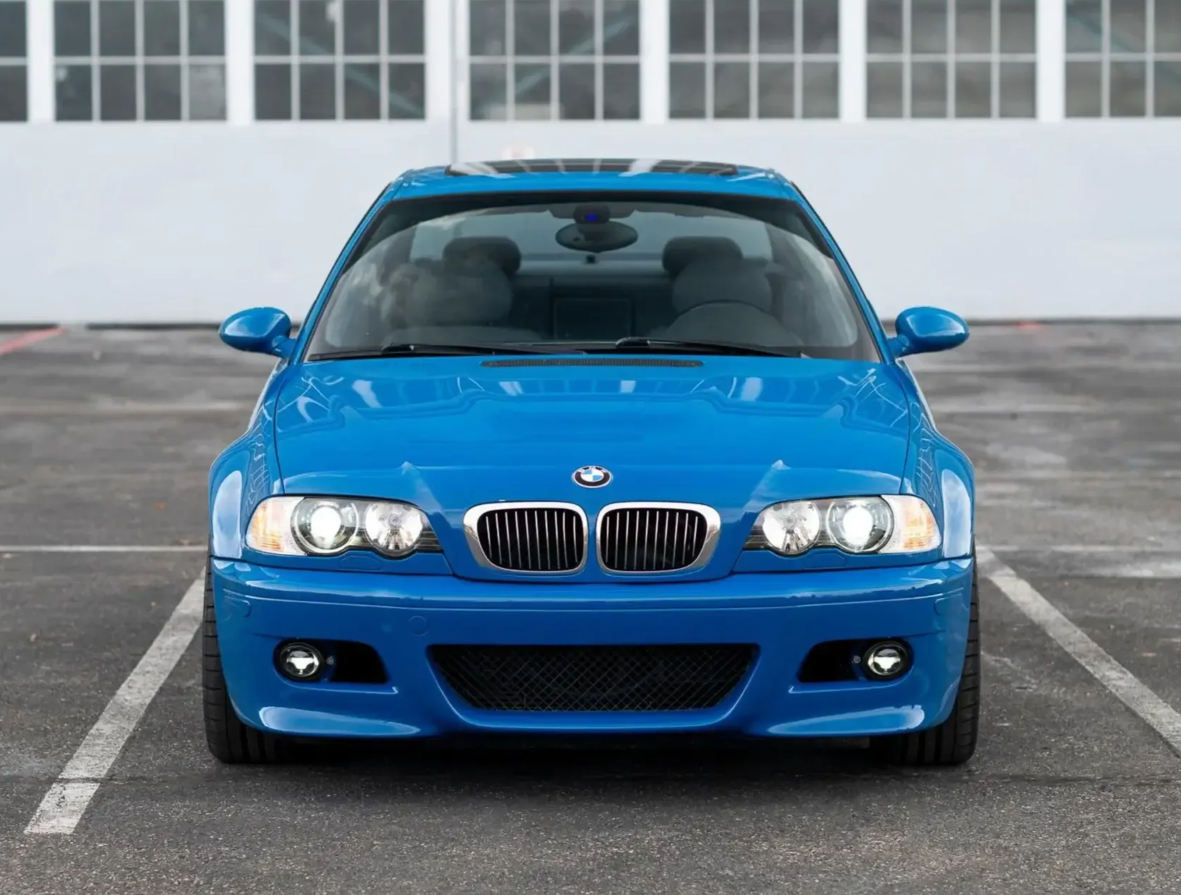 Blue BMW sedan parked front-facing in a lot with a garage door background