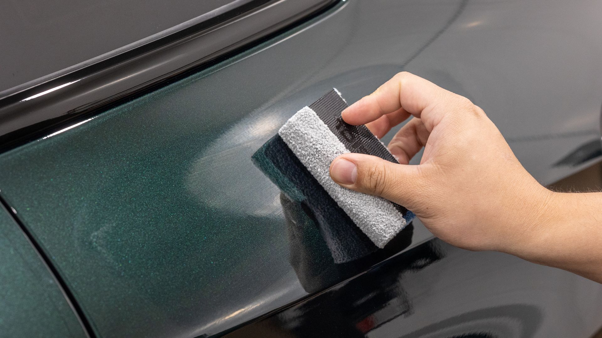 Hand sanding a dark green car panel with a small sanding block