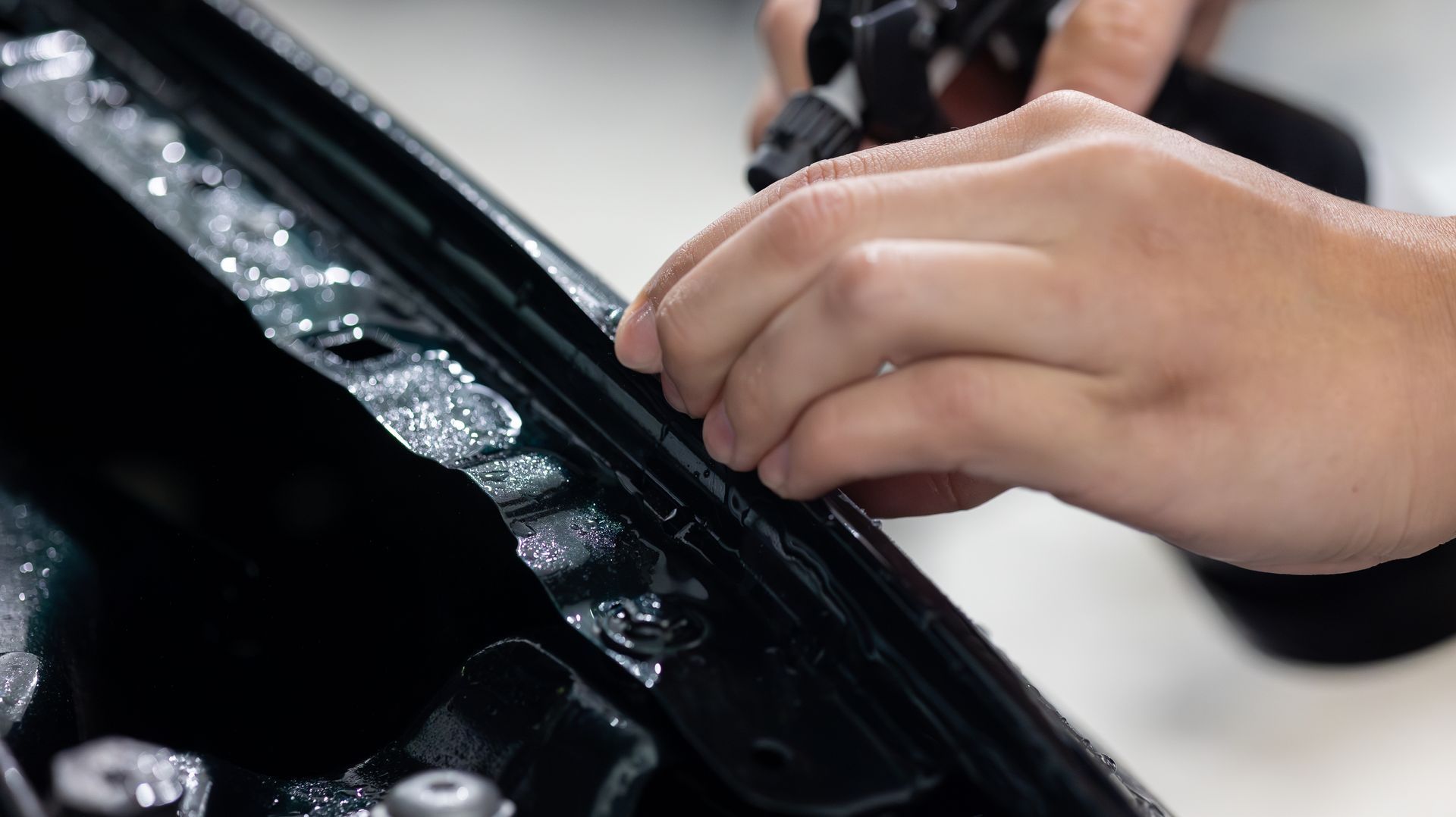 Hands adjusting a glossy black car panel with bubble wrap inside a workshop