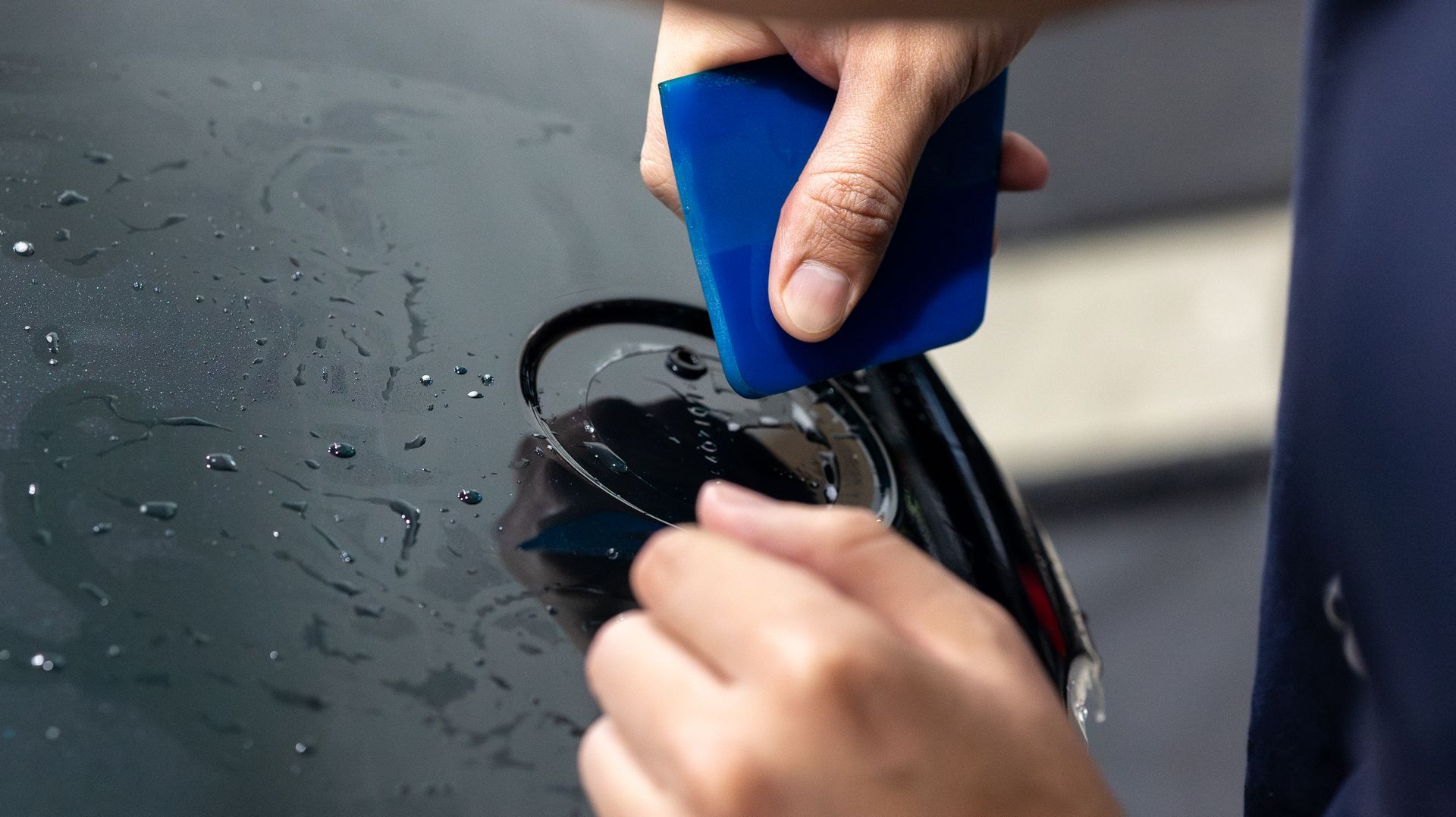 Hands using a blue applicator to apply coating to a black car surface