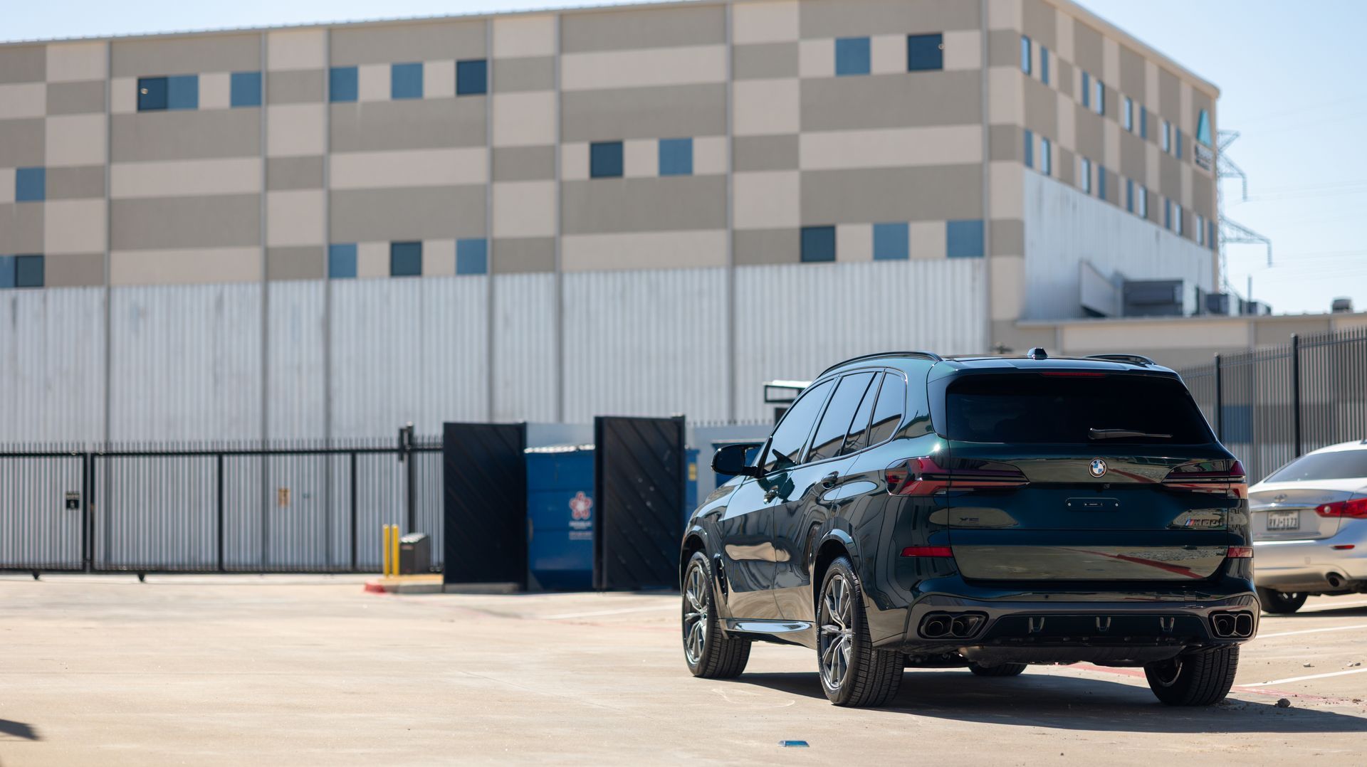 Black SUV parked outside a beige industrial building with blue windows and a metal fence