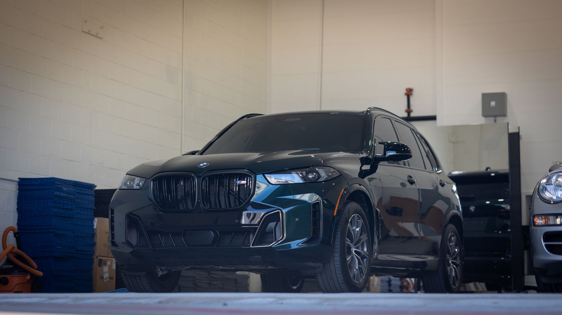 Dark SUV parked inside a garage or workshop, with another vehicle partially visible beside it.