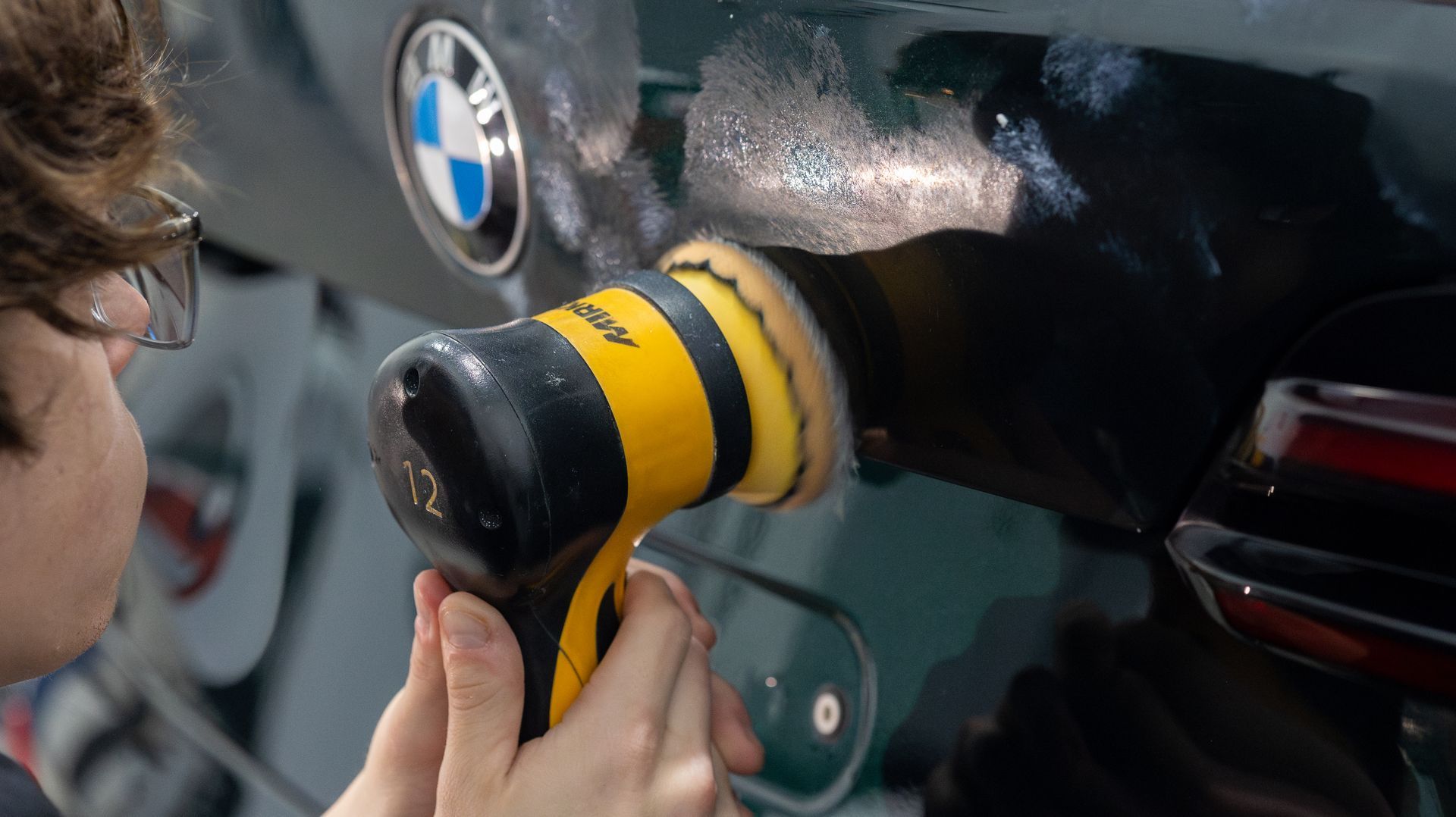 Person using a yellow polishing tool on a black BMW car panel