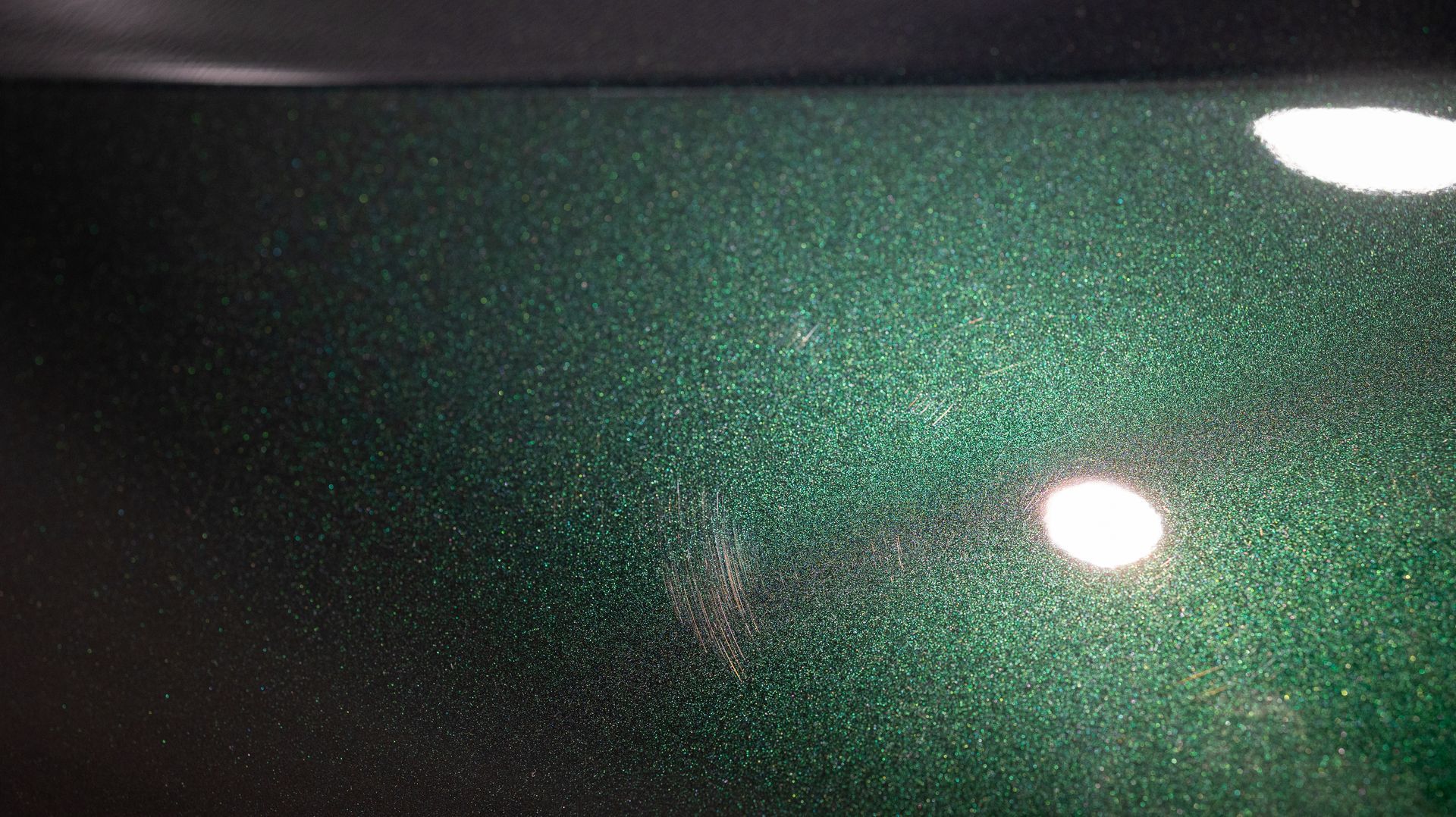 Close-up of dark green metallic surface with two bright light reflections