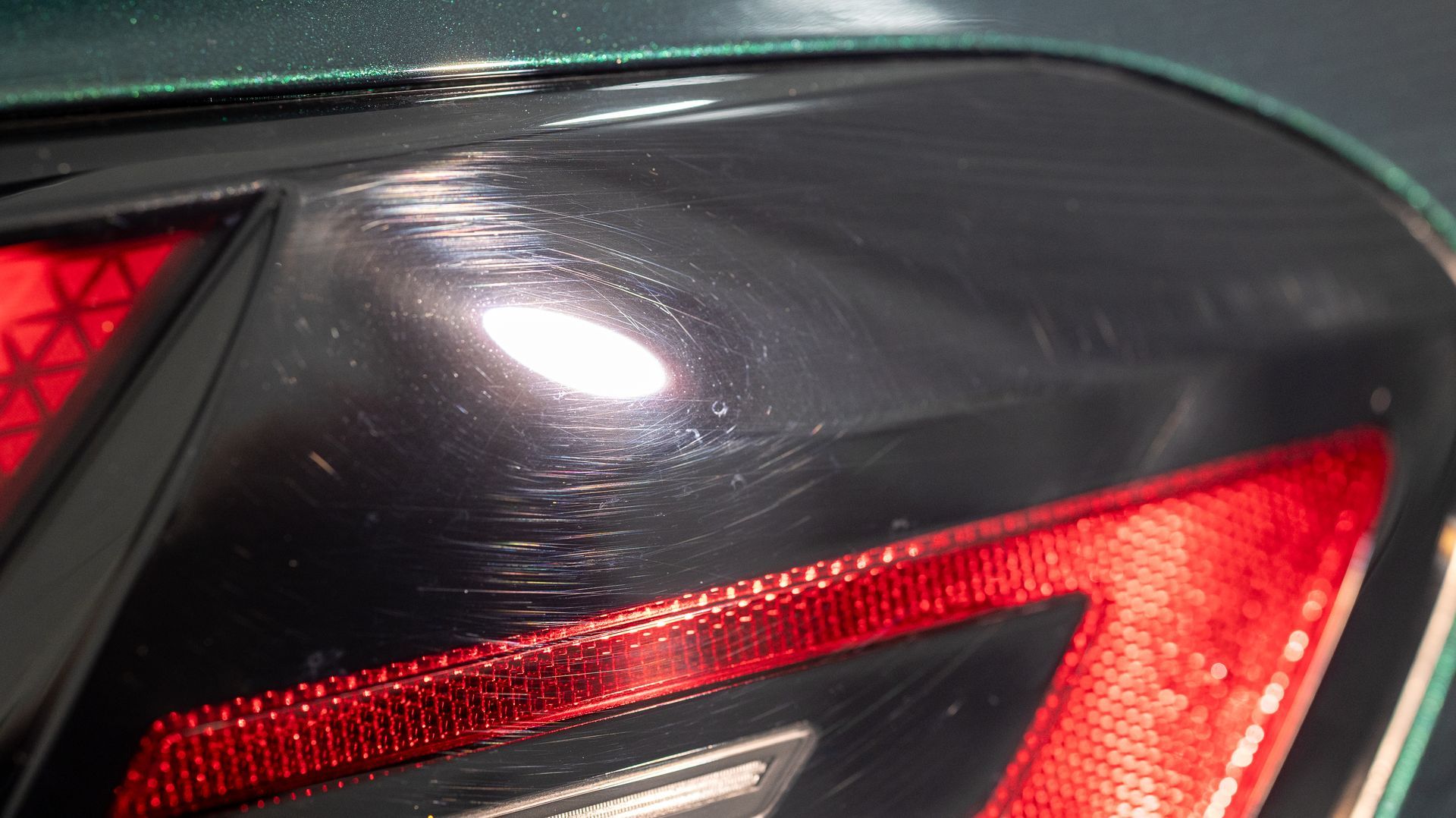 Close-up of a dark car’s rear taillight with red lens and glossy paint.