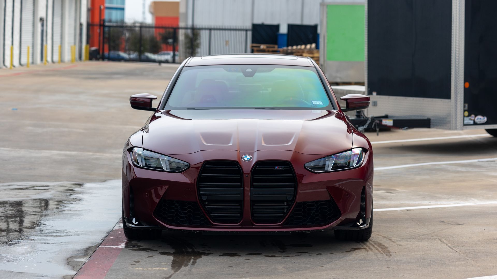 Maroon sports car parked on a wet industrial lot, front view.