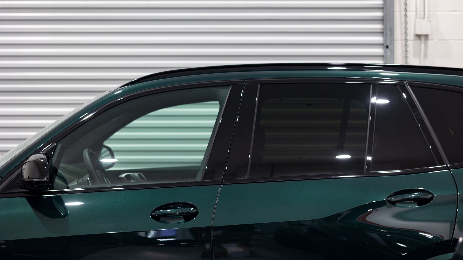 Dark green car parked in front of a white corrugated metal garage door