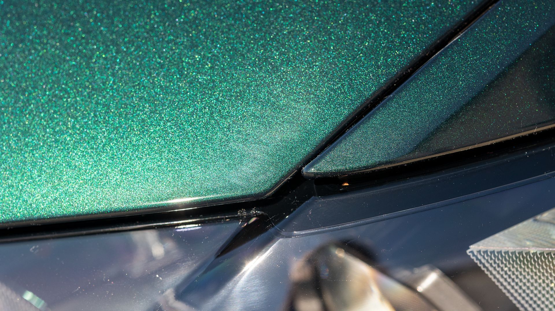 Close-up of teal car body panel with black trim and a scratched or dented seam