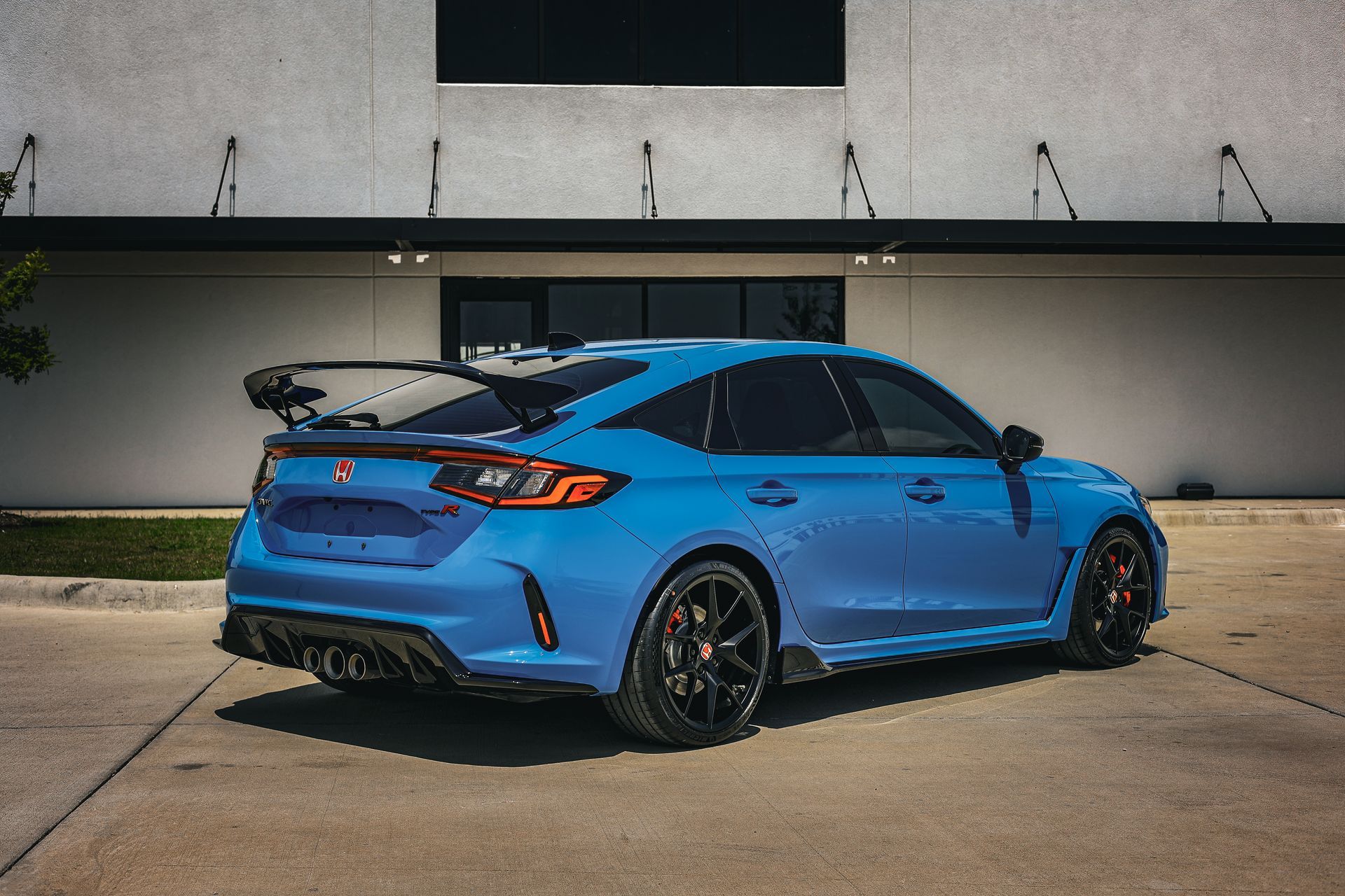 A bright blue Honda Civic Type R hatchback parked on a paved lot in front of a white building.