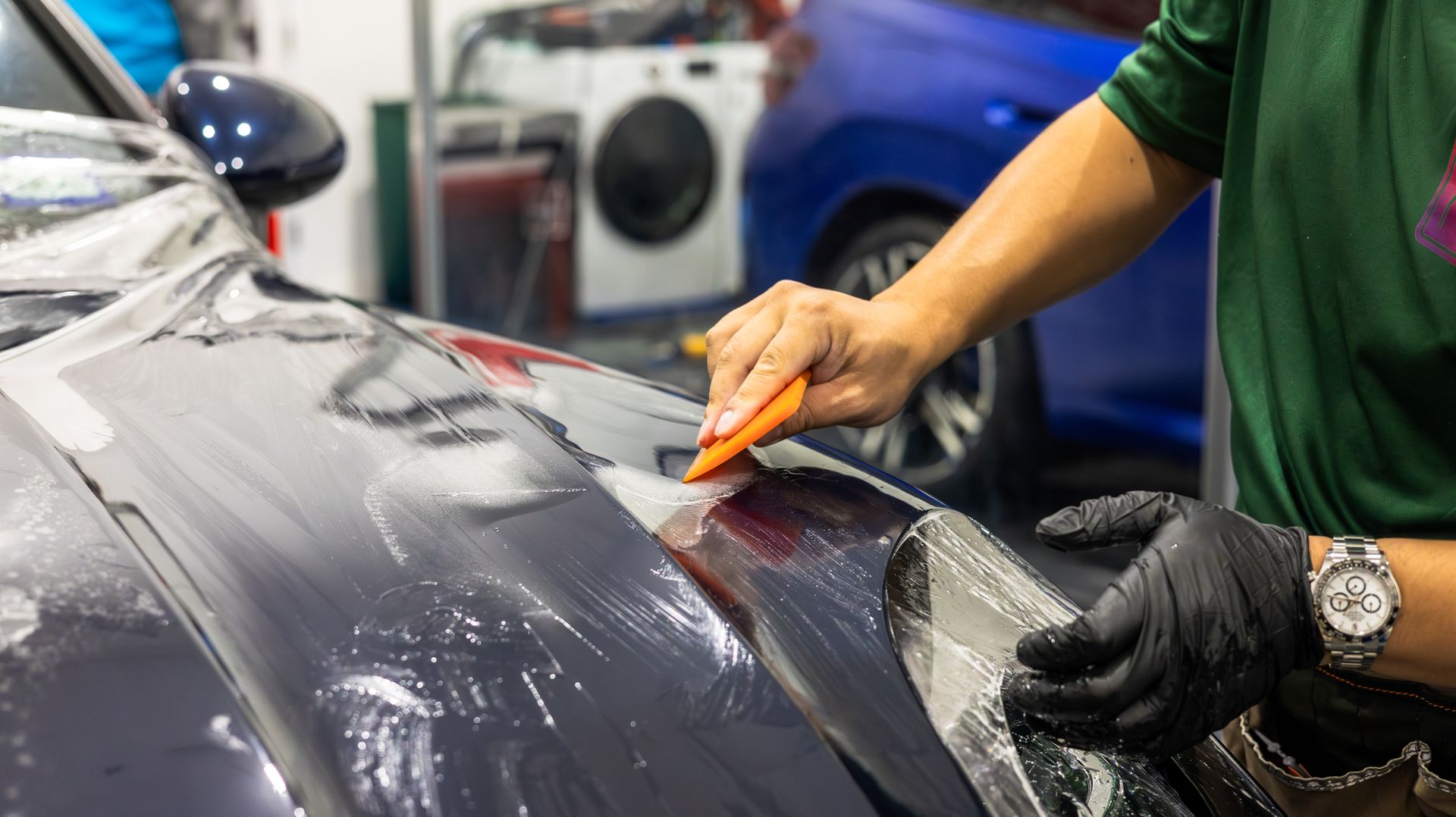 Person applying a clear film to a black car hood in a garage