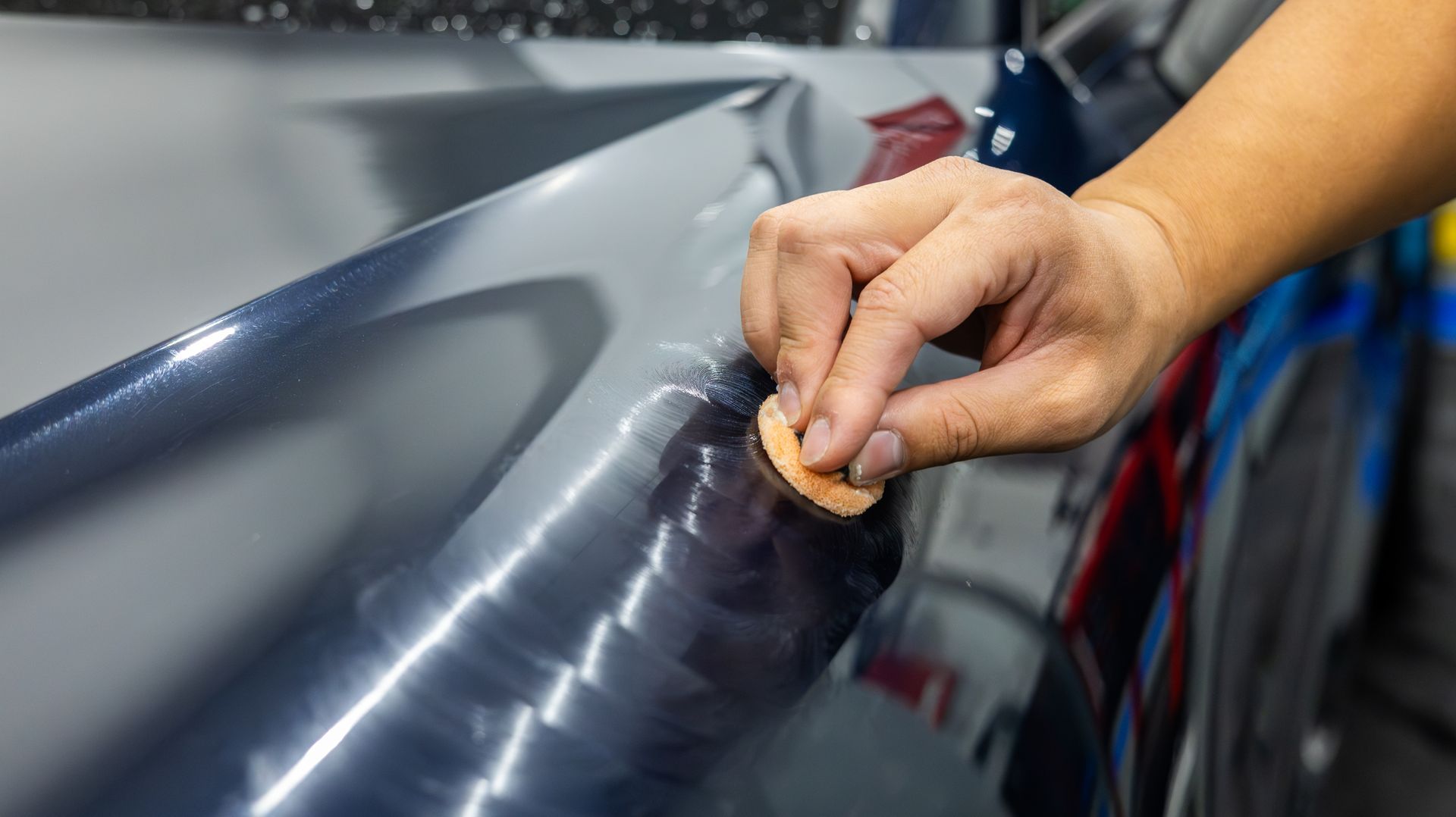 Hand polishing a dark car panel with a cloth, creating a glossy finish