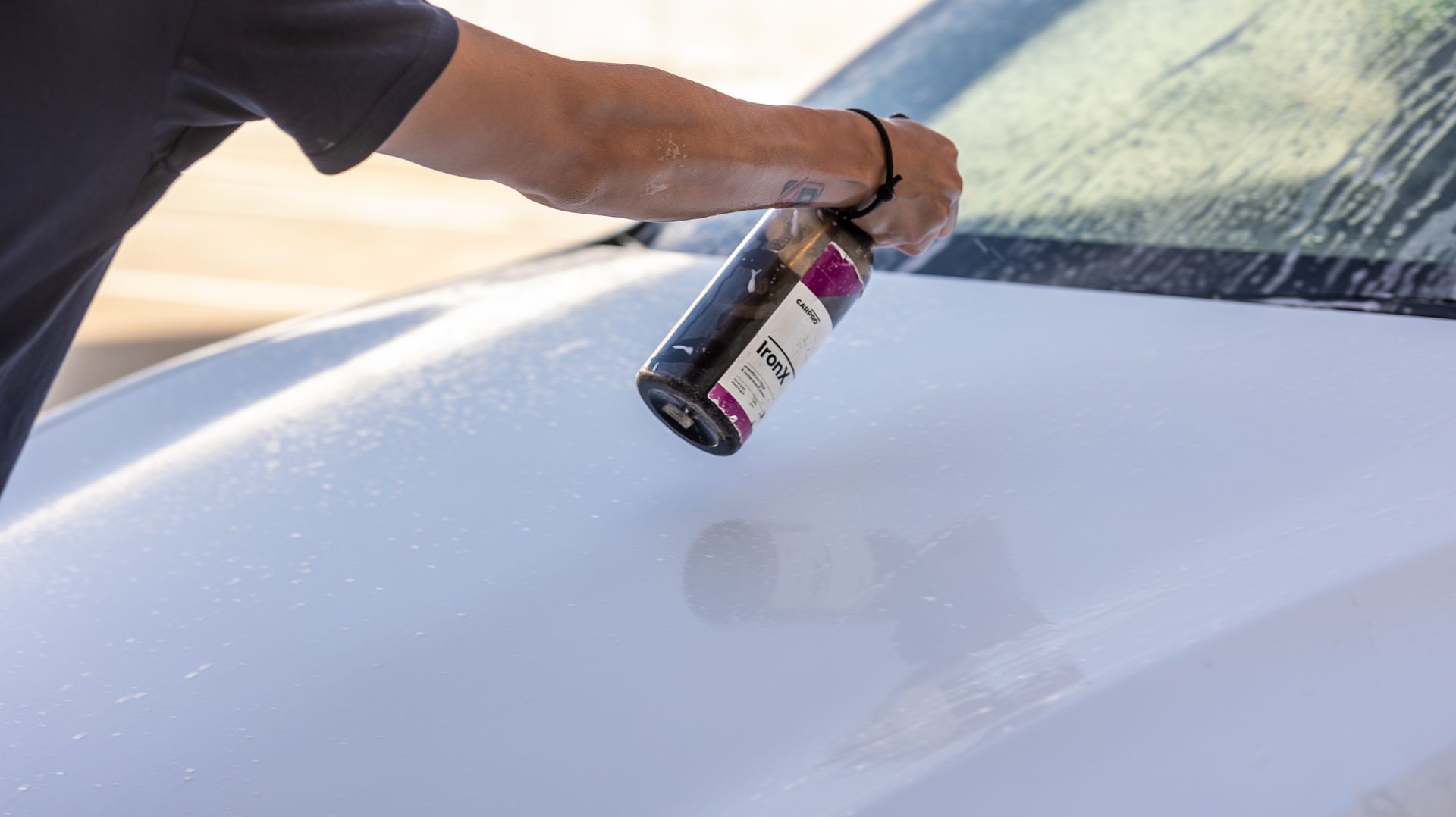 A person is washing a white car with a spray bottle.