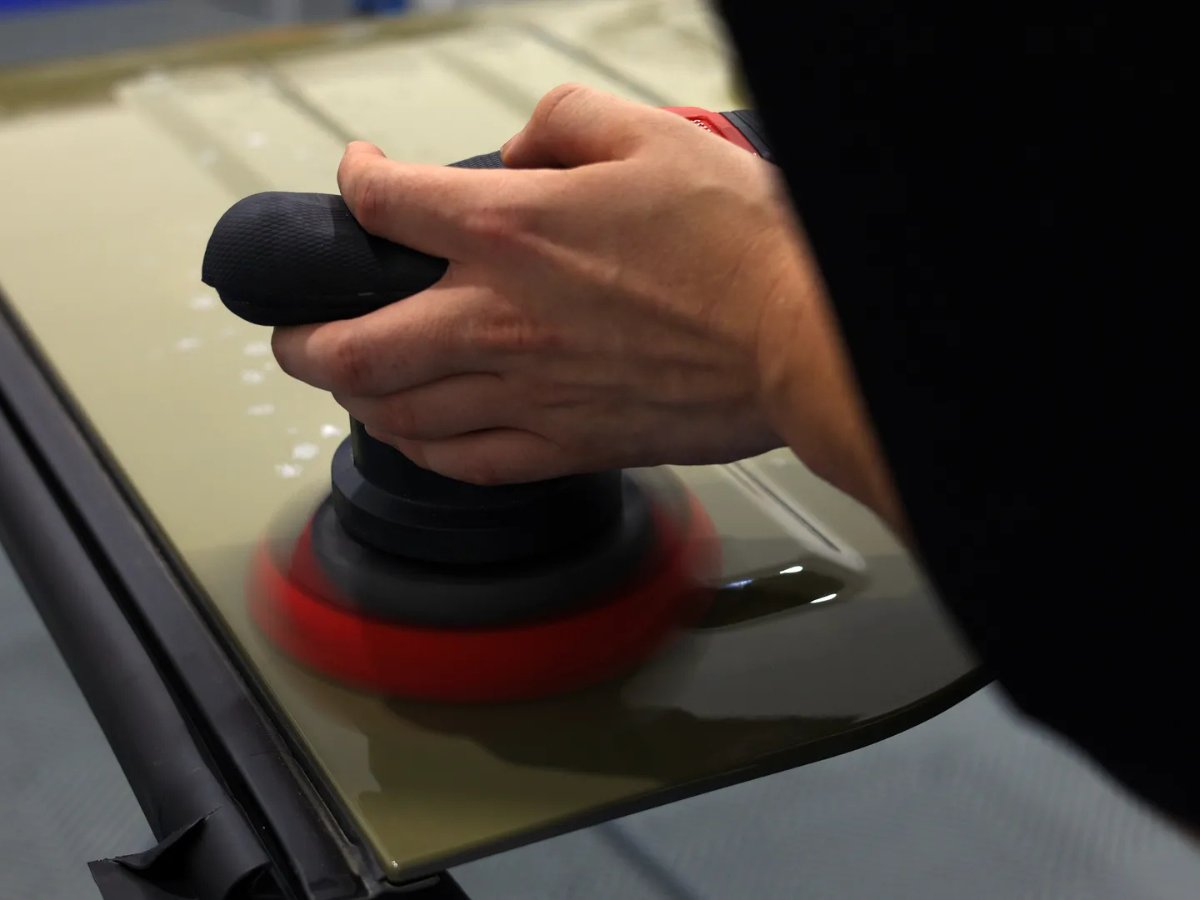 Technician performing paint correction on olive green vehicle panel using dual action orbital polisher