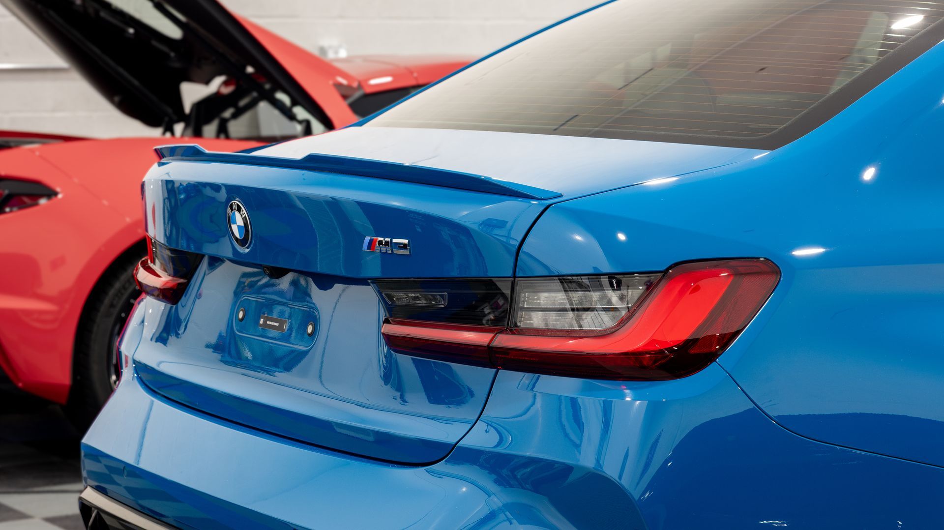 Rear view of a blue sports sedan with a rear spoiler, parked beside a red car