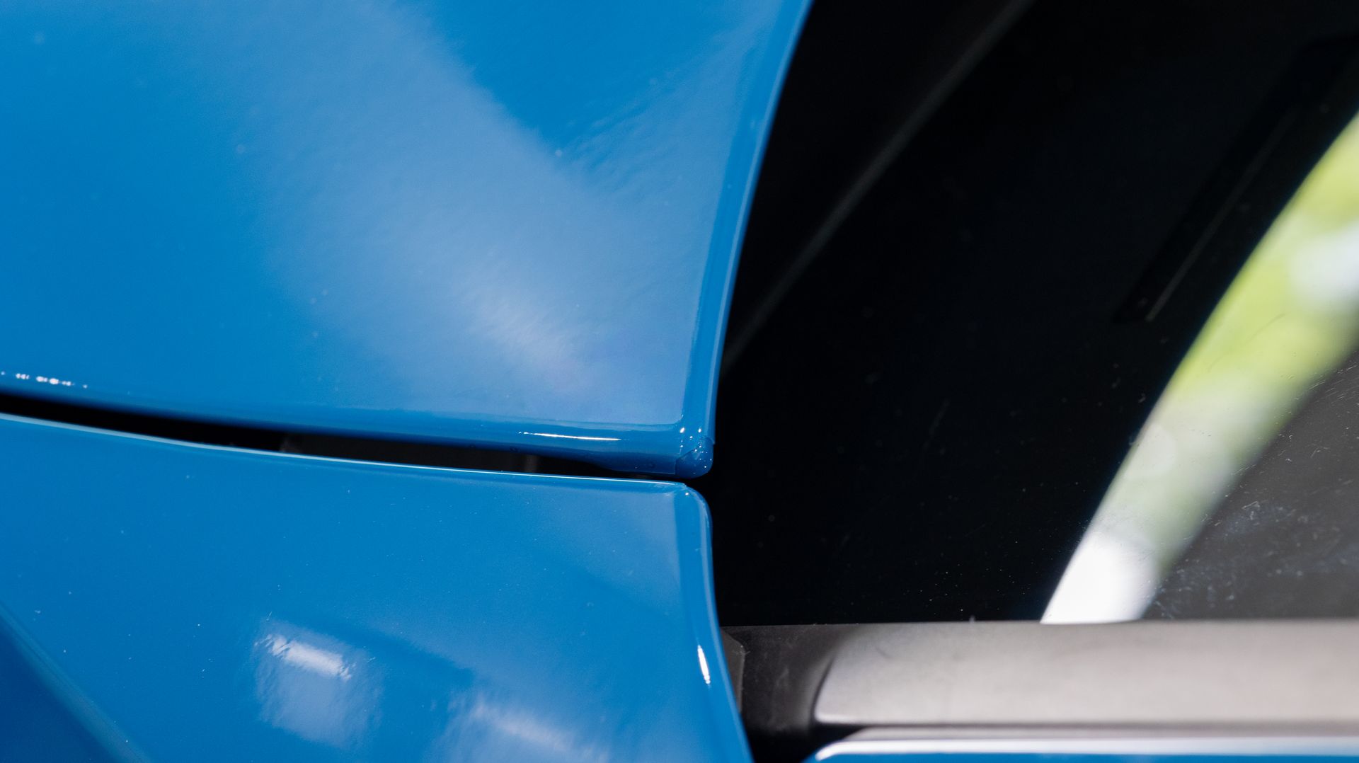 Close-up of a blue car body panel and black window trim with silver accent