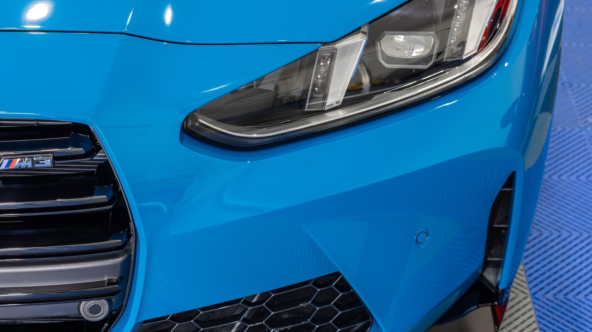 Close-up of a bright blue car front with headlight, grille, and bumper detail