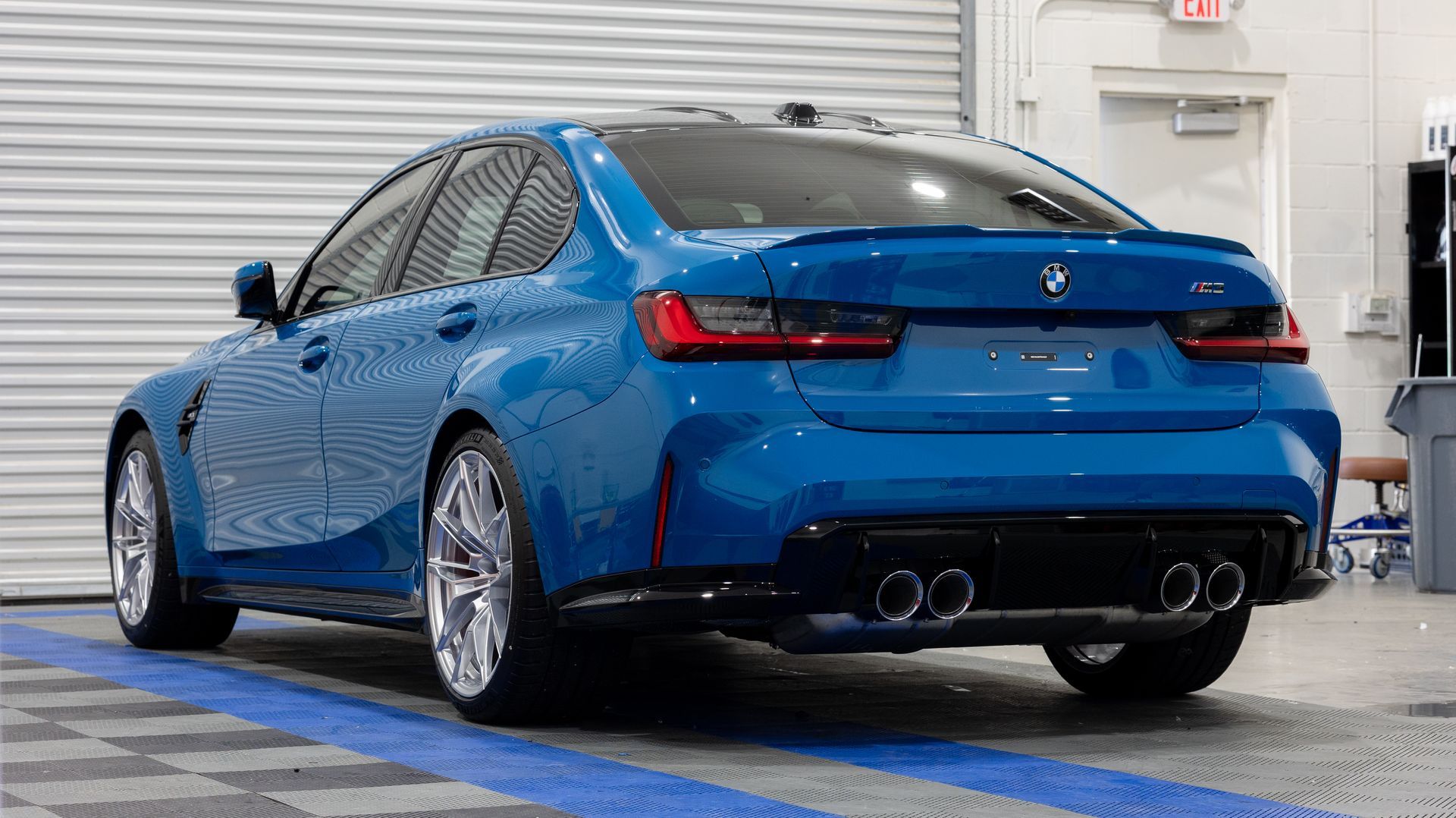Blue sports sedan in a garage, rear three-quarter view with polished wheels and quad exhausts.