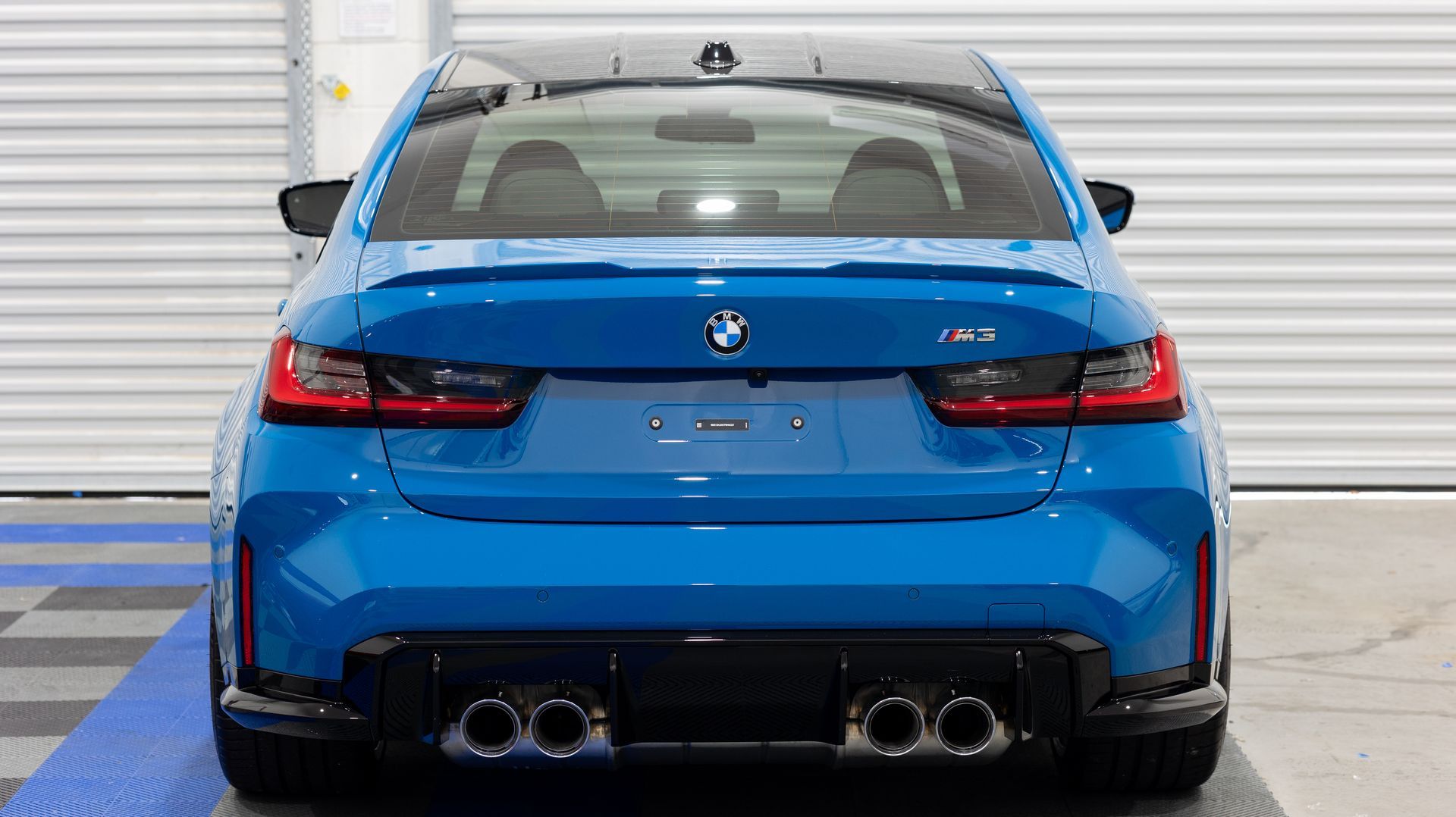 Rear view of a blue BMW sports car parked indoors against a white garage door.