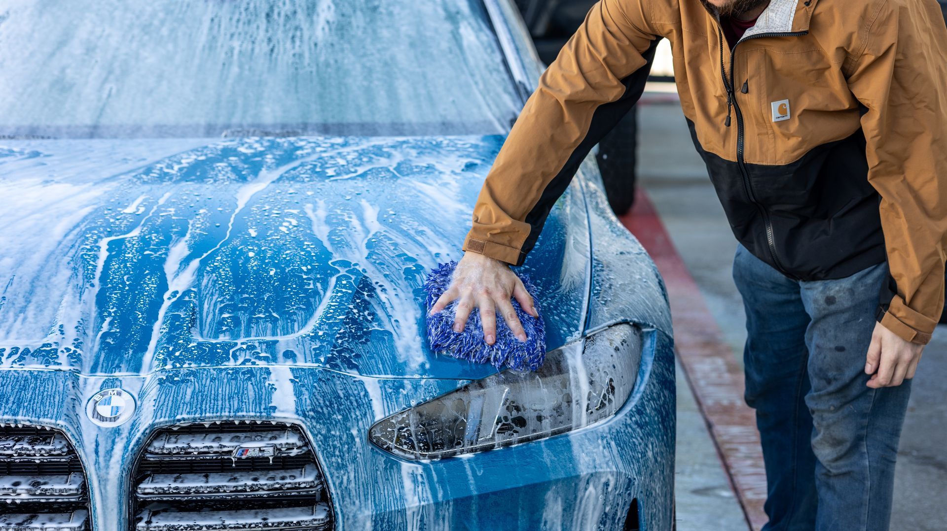 Person washing a blue car covered in soap suds at a car wash