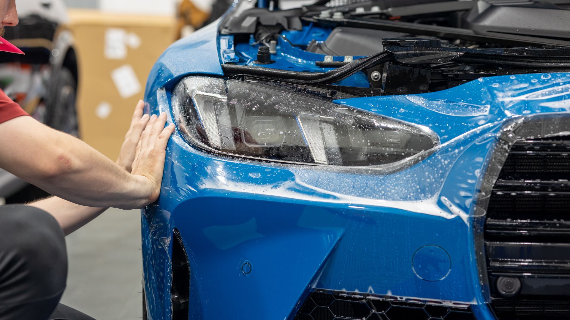 Person wiping a blue sports car’s front fender and headlight in a garage