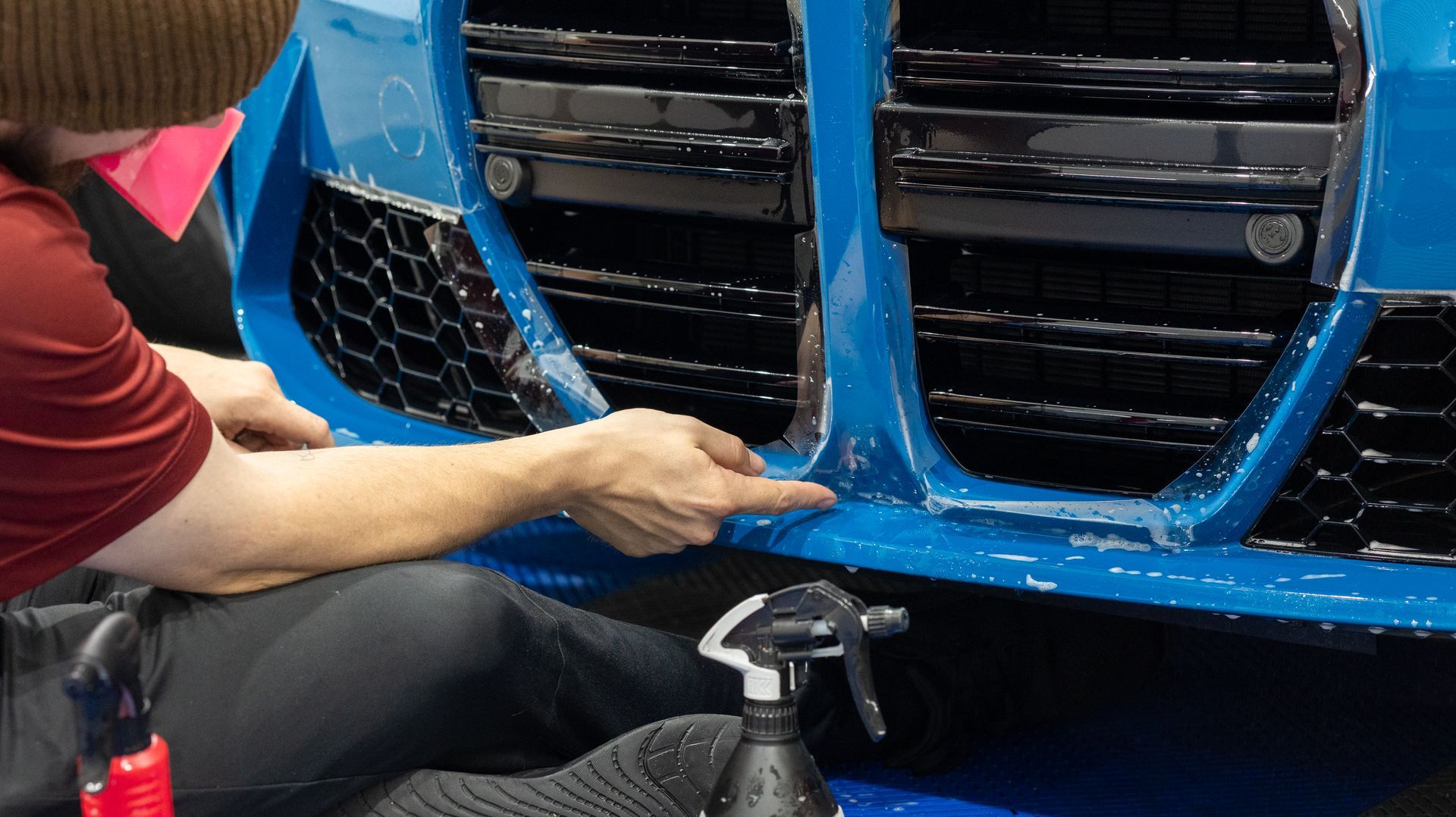 Person cleaning a blue car grille with a cloth inside a vehicle shop