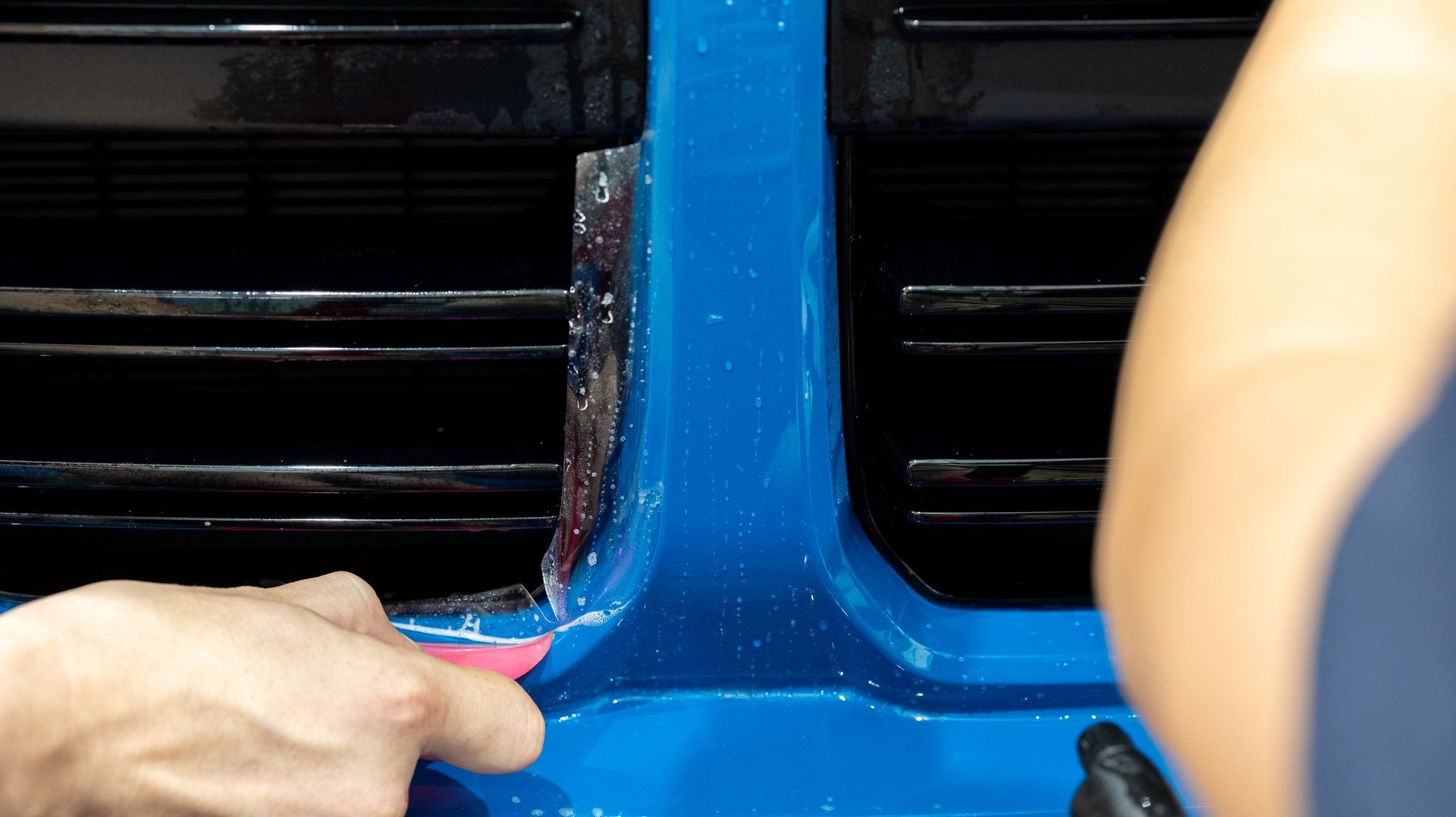Hands peeling blue tape from a glossy blue and black surface