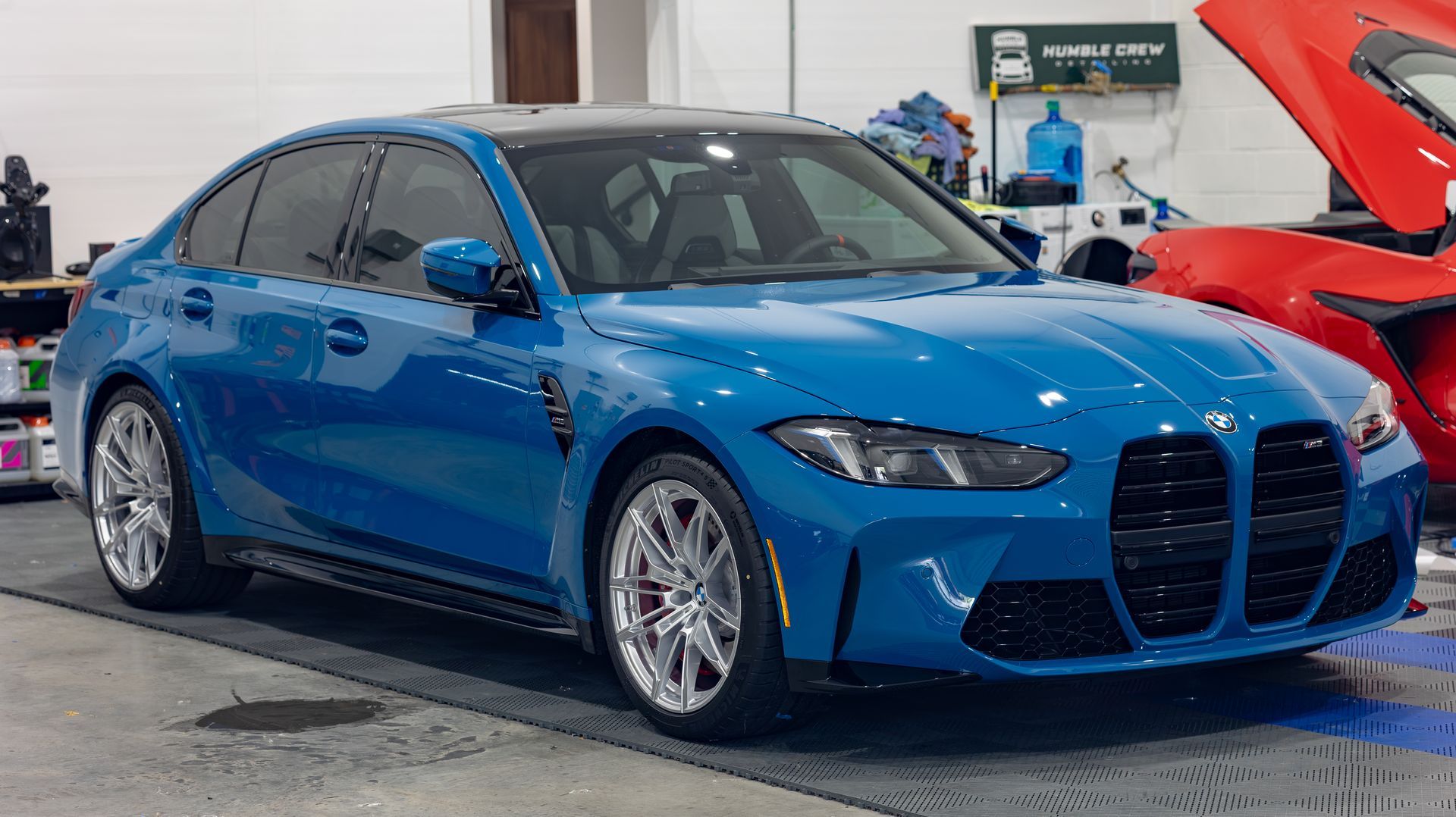 Blue BMW sedan in an auto shop with a red car hood open beside it