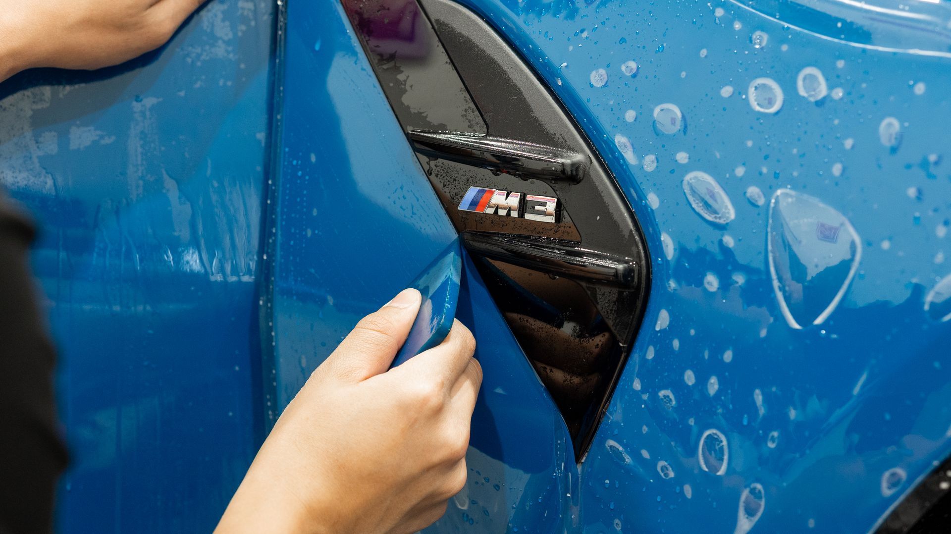 Hand opening a blue car’s charging port cover on a BMW M model