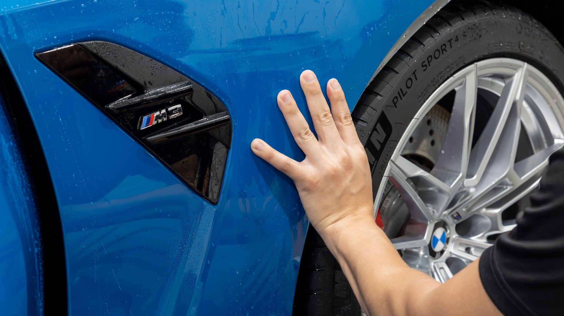 Hand touching a blue BMW’s fender near the wheel