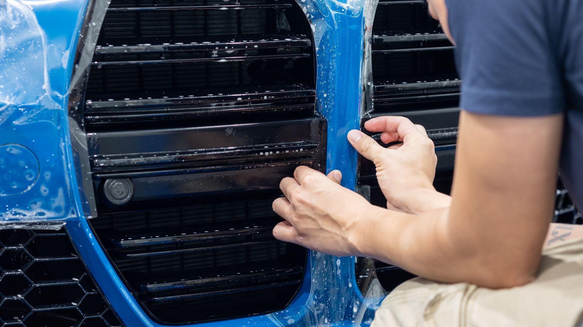 Person working on a large black vent wrapped in blue protective film
