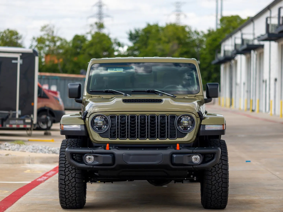 Olive green Jeep Wrangler Rubicon with round LED headlights and all-terrain tires front view in park