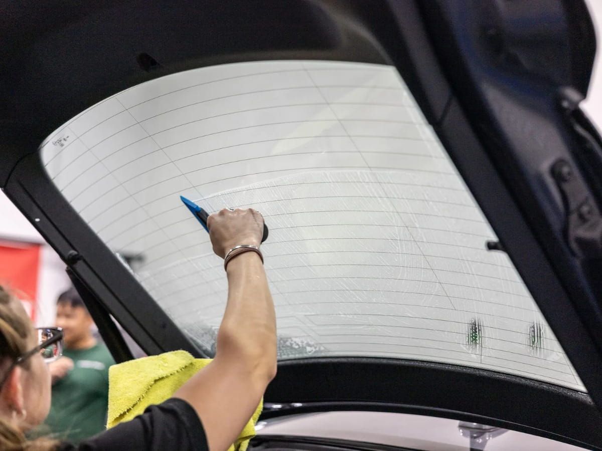 Technician preparing window tint film on a vehicle's rear windshield.