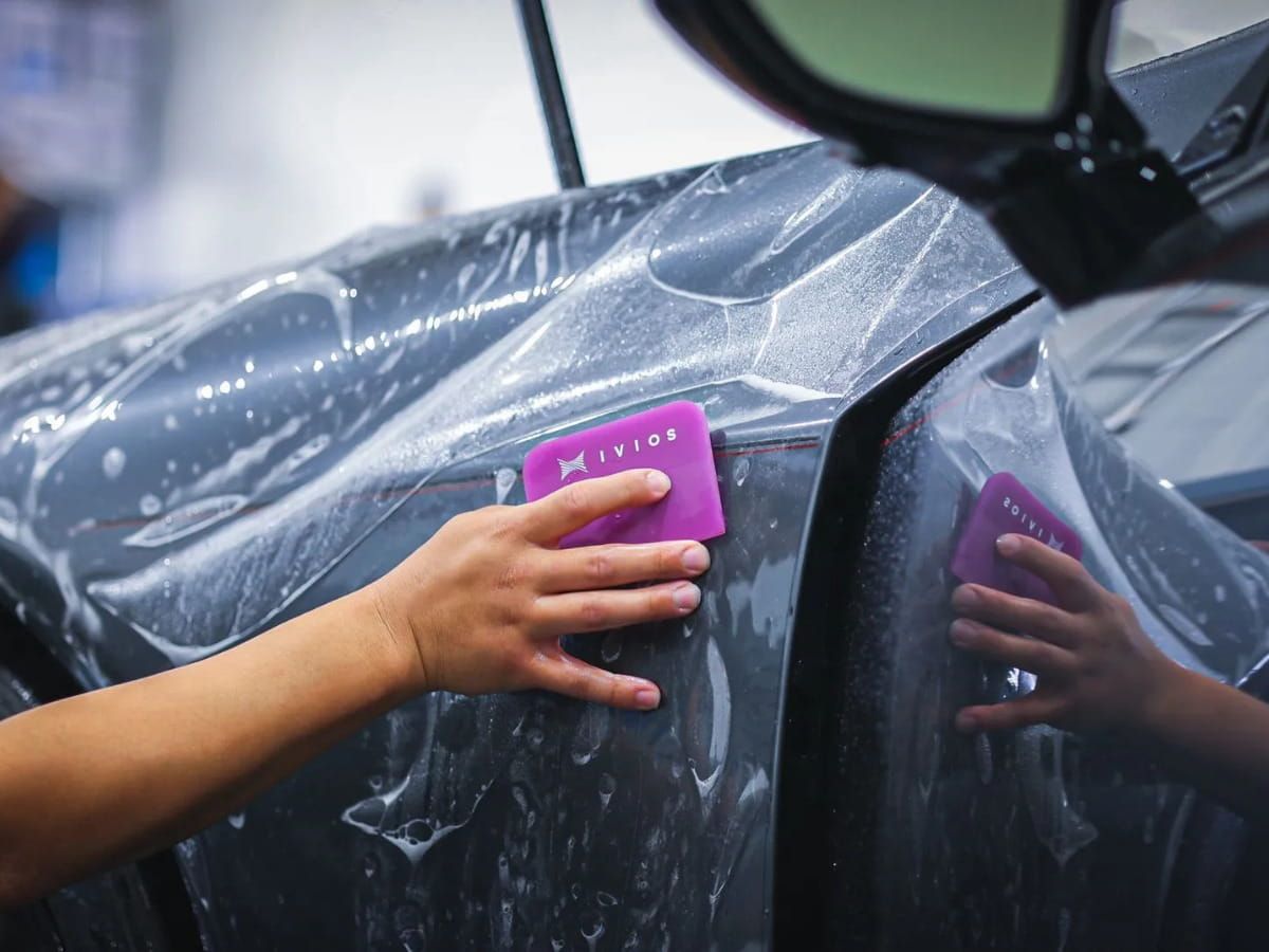 Technician installing paint protection film on the front fender of a gray vehicle.