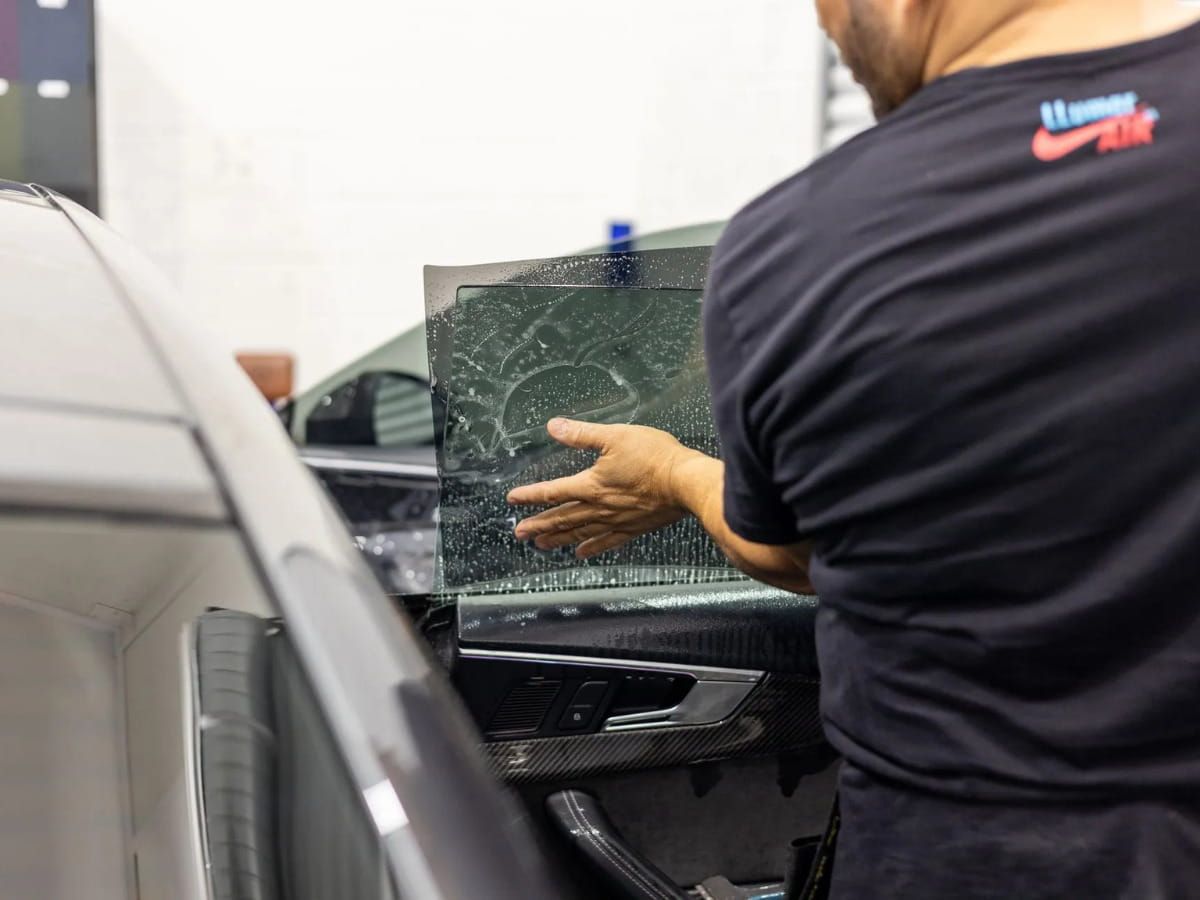 Technician applying window tint film to a vehicle side window.