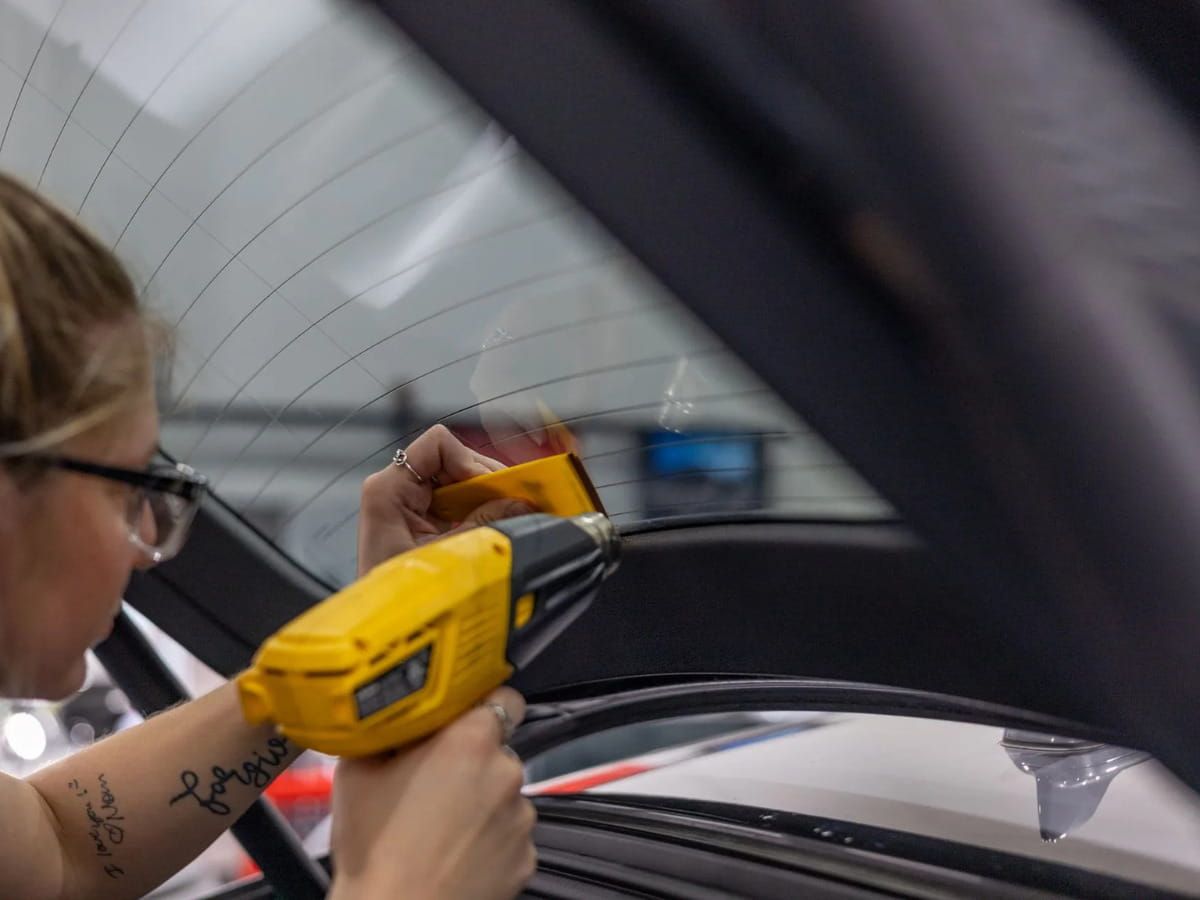 Technician using a heat gun during rear windshield tint installation.