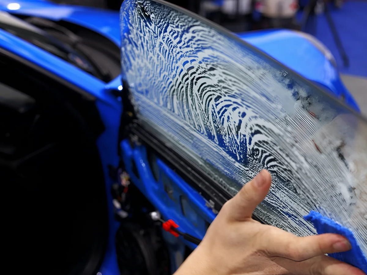 Window tint film being installed on the side window of a blue vehicle.
