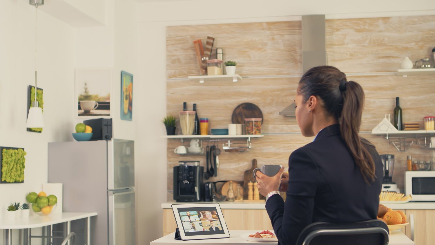 Person working at a laptop in a bright kitchen, with shelves, coffee setup, and plants in the background