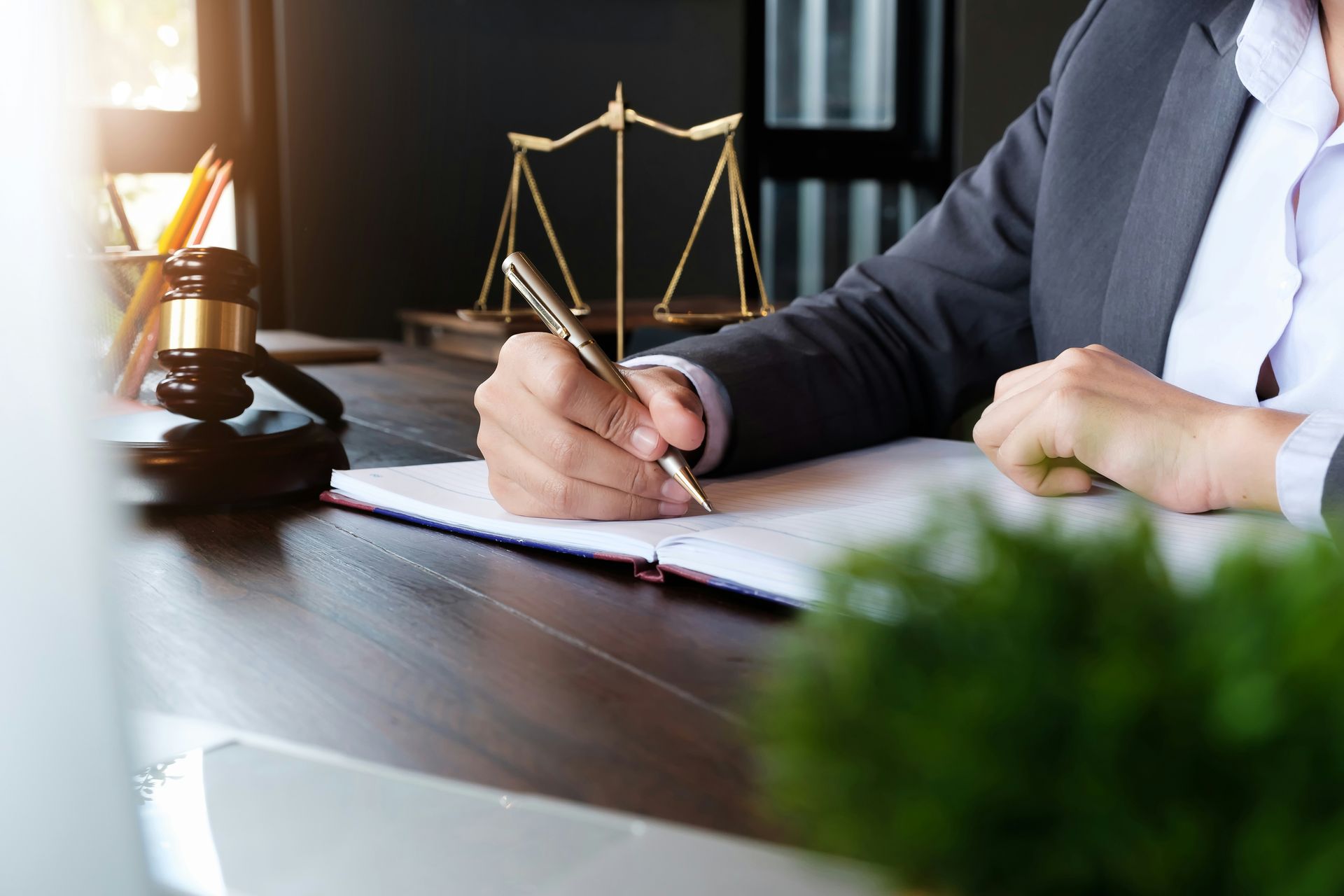 Lawyer signing documents at a desk with a scales of justice statue